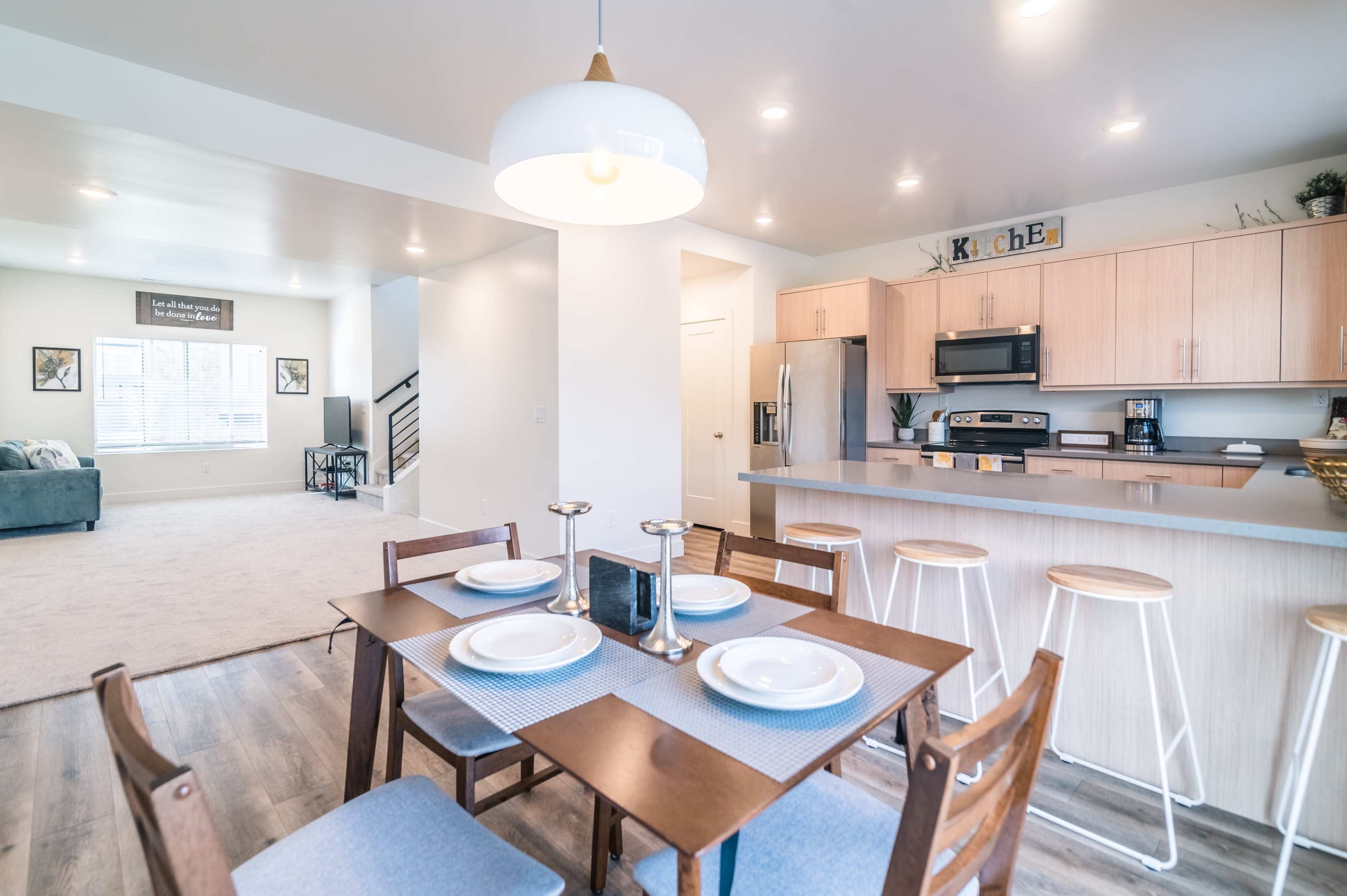A kitchen and dining area with a table set for four, modern cabinetry, and a living room visible in the background.