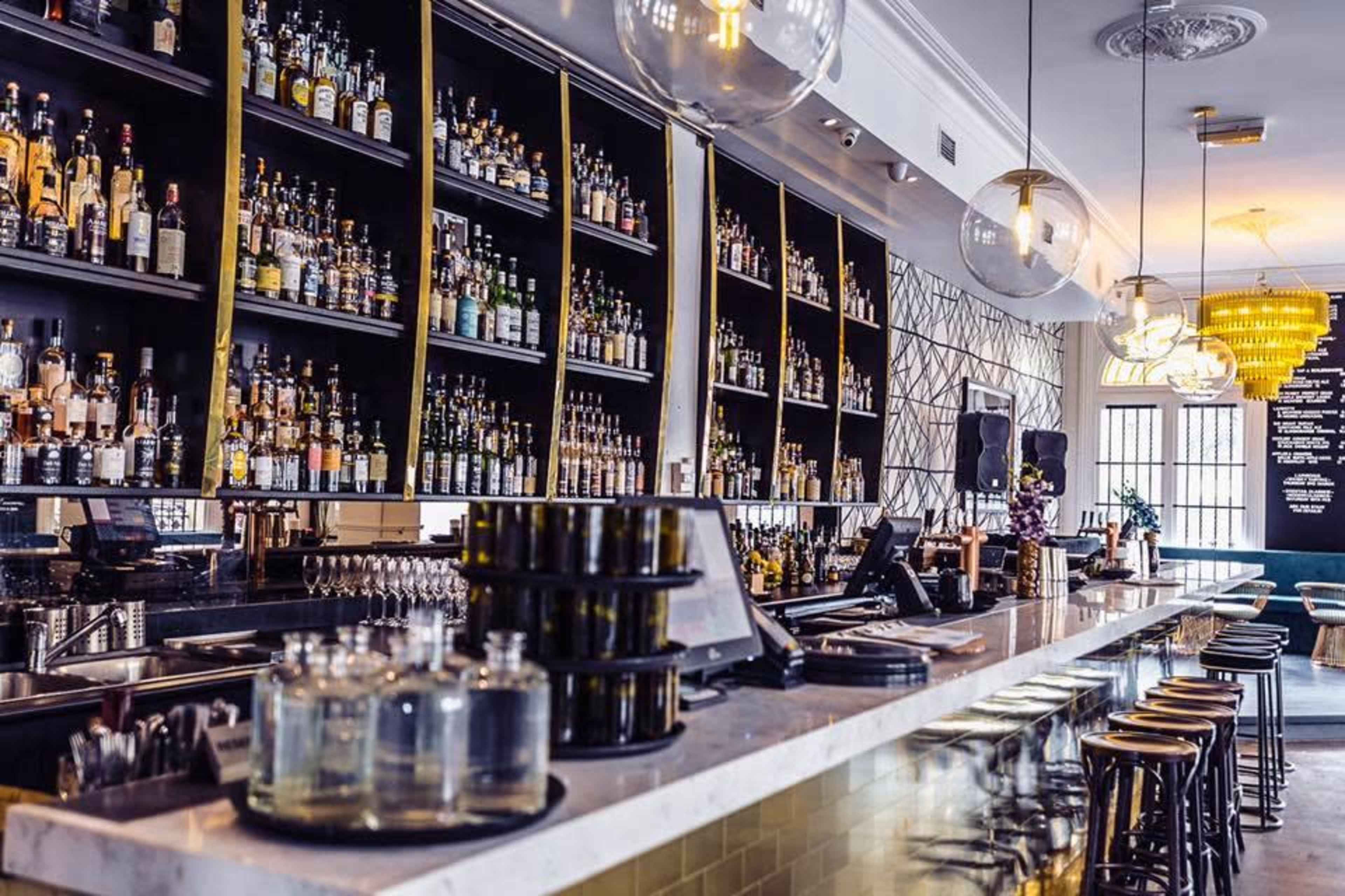 A sleek, modern bar features a well-stocked liquor shelf, polished counter, and contemporary lighting.