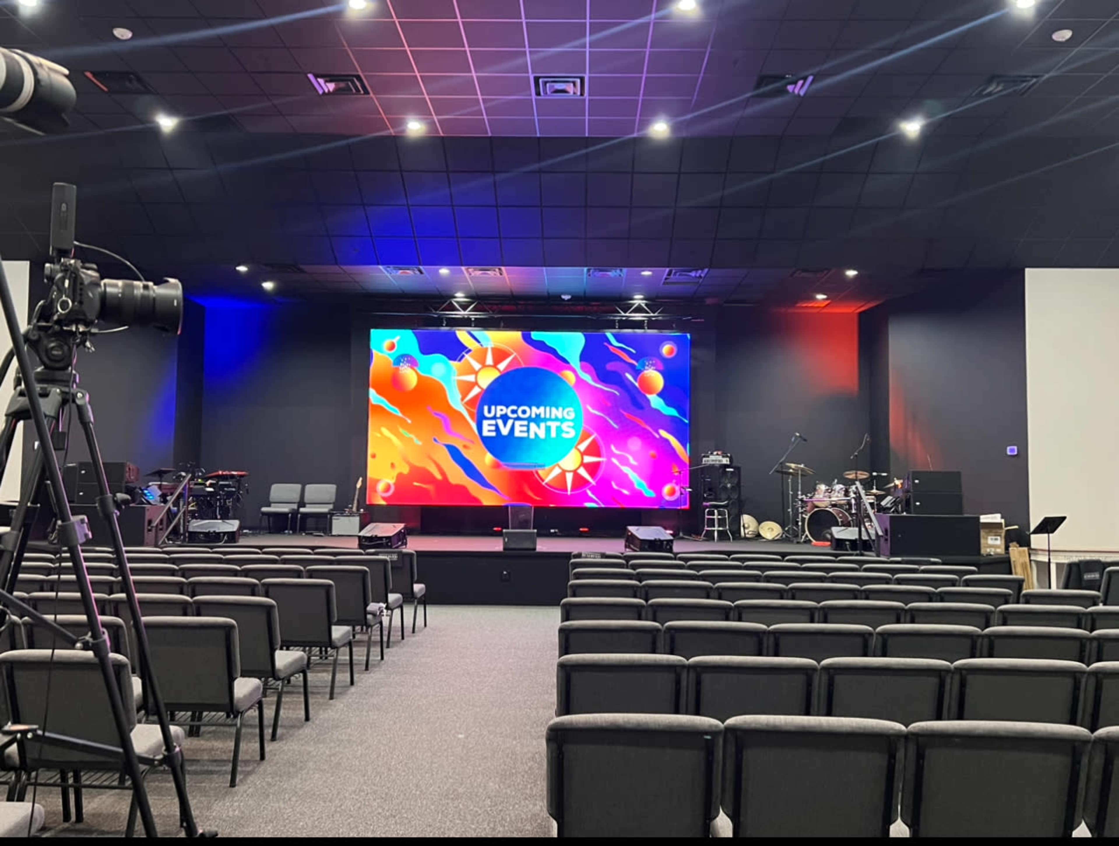 An auditorium set up for an event, featuring a large screen displaying "UPCOMING EVENTS" and rows of chairs facing the stage.