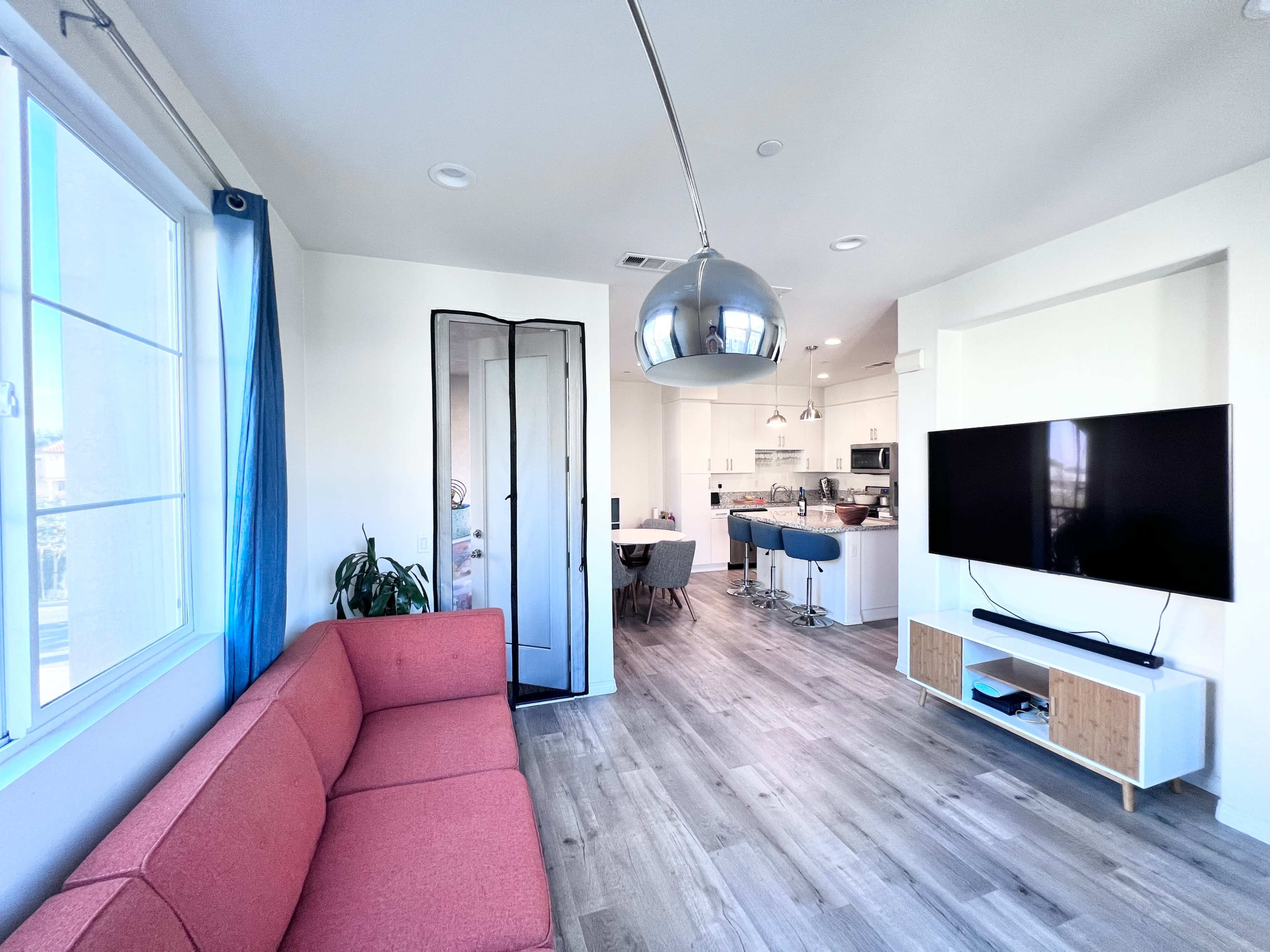 A modern living room features a red couch, a large TV mounted on the wall, and an open kitchen area visible in the background.