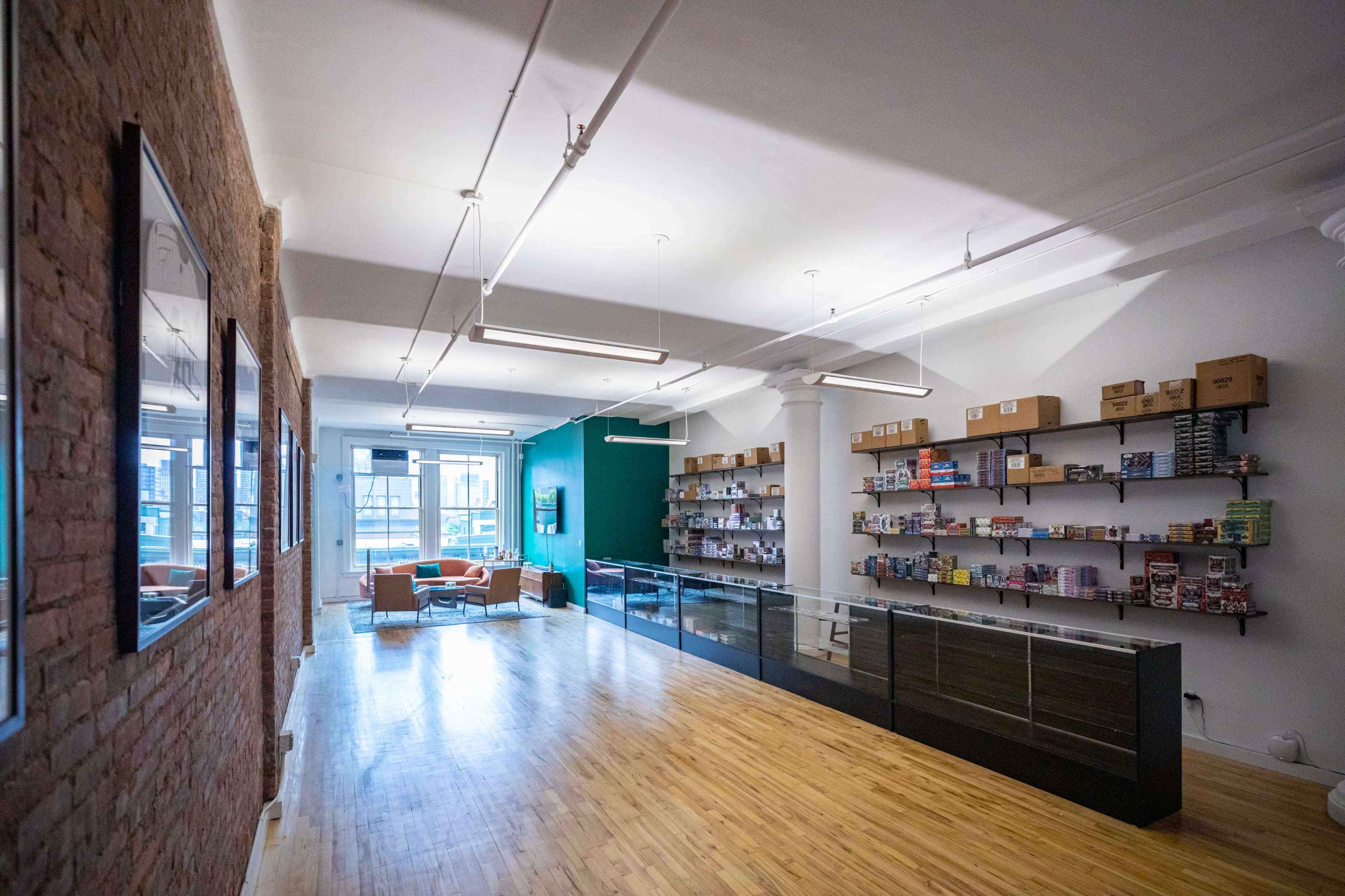 An empty retail space features wooden flooring, exposed brick walls, and shelves filled with products along one side, with a glass display case in front.