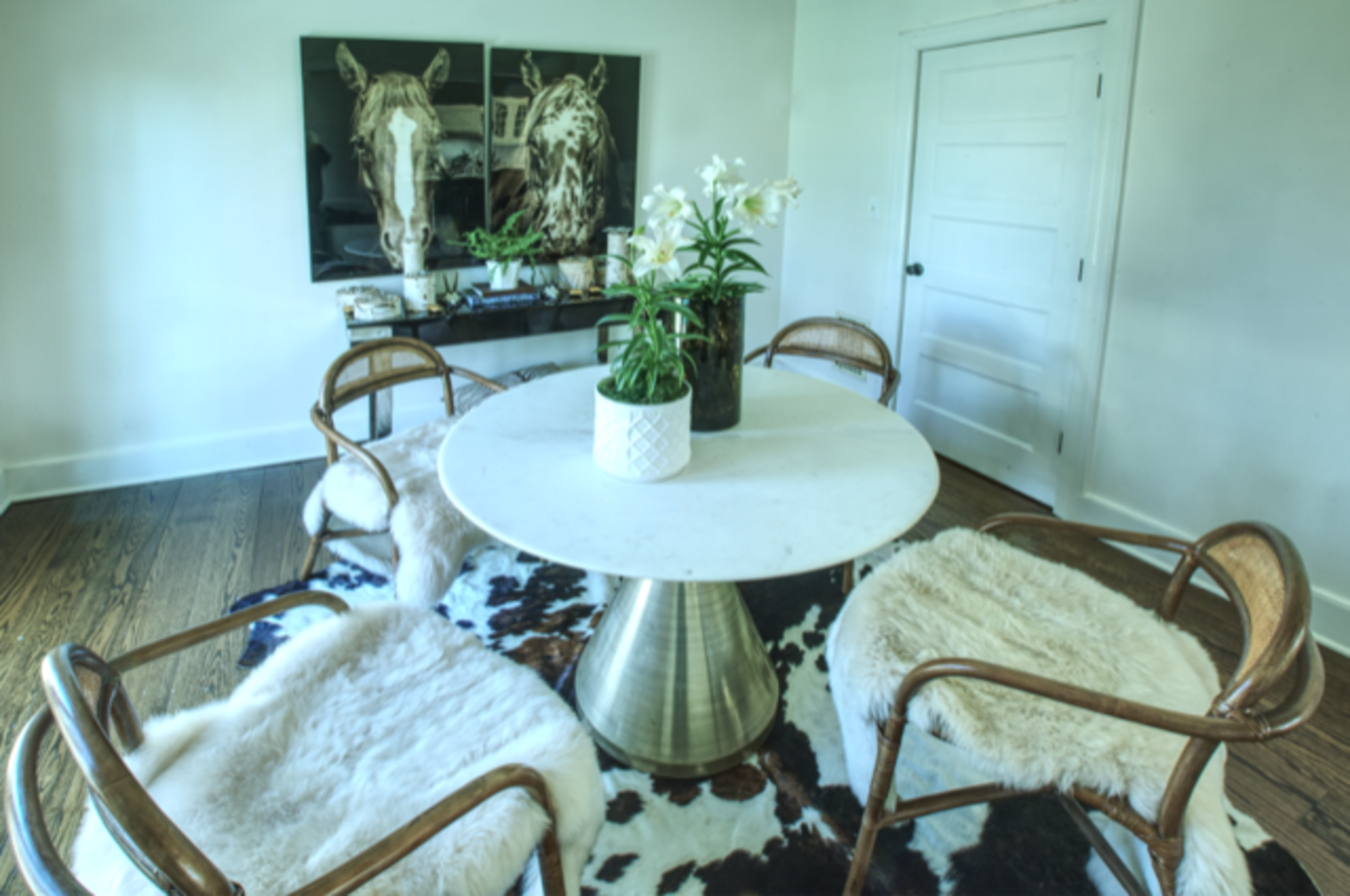 A round table with a marble top is surrounded by four curved wooden chairs on a cowhide rug in a well-lit room.