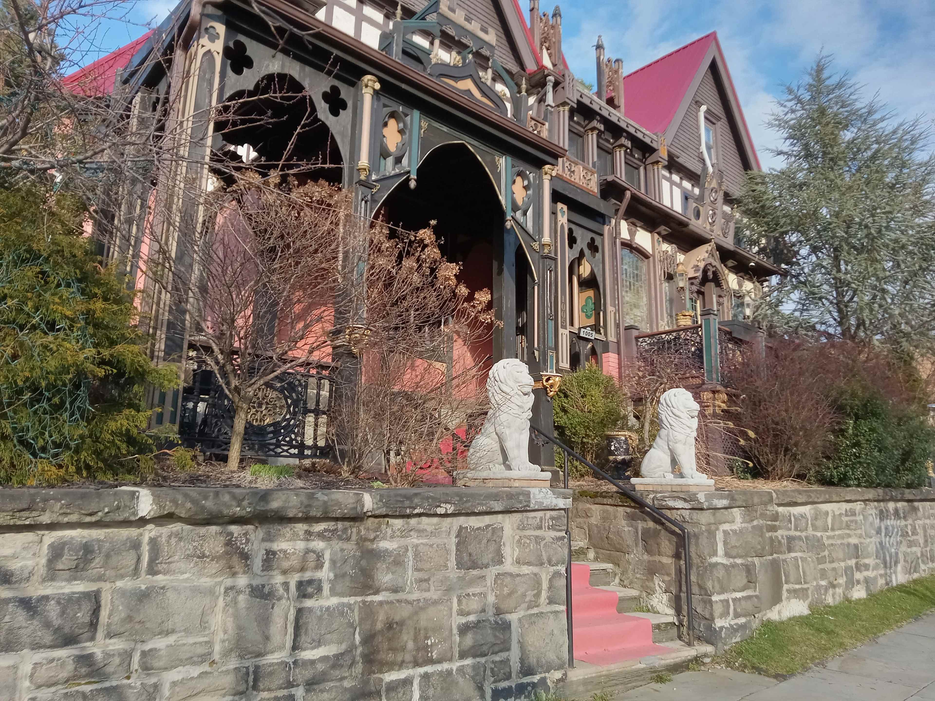 A large Victorian-style house with ornate architecture, featuring a red roof and stone lion statues flanking its entrance.