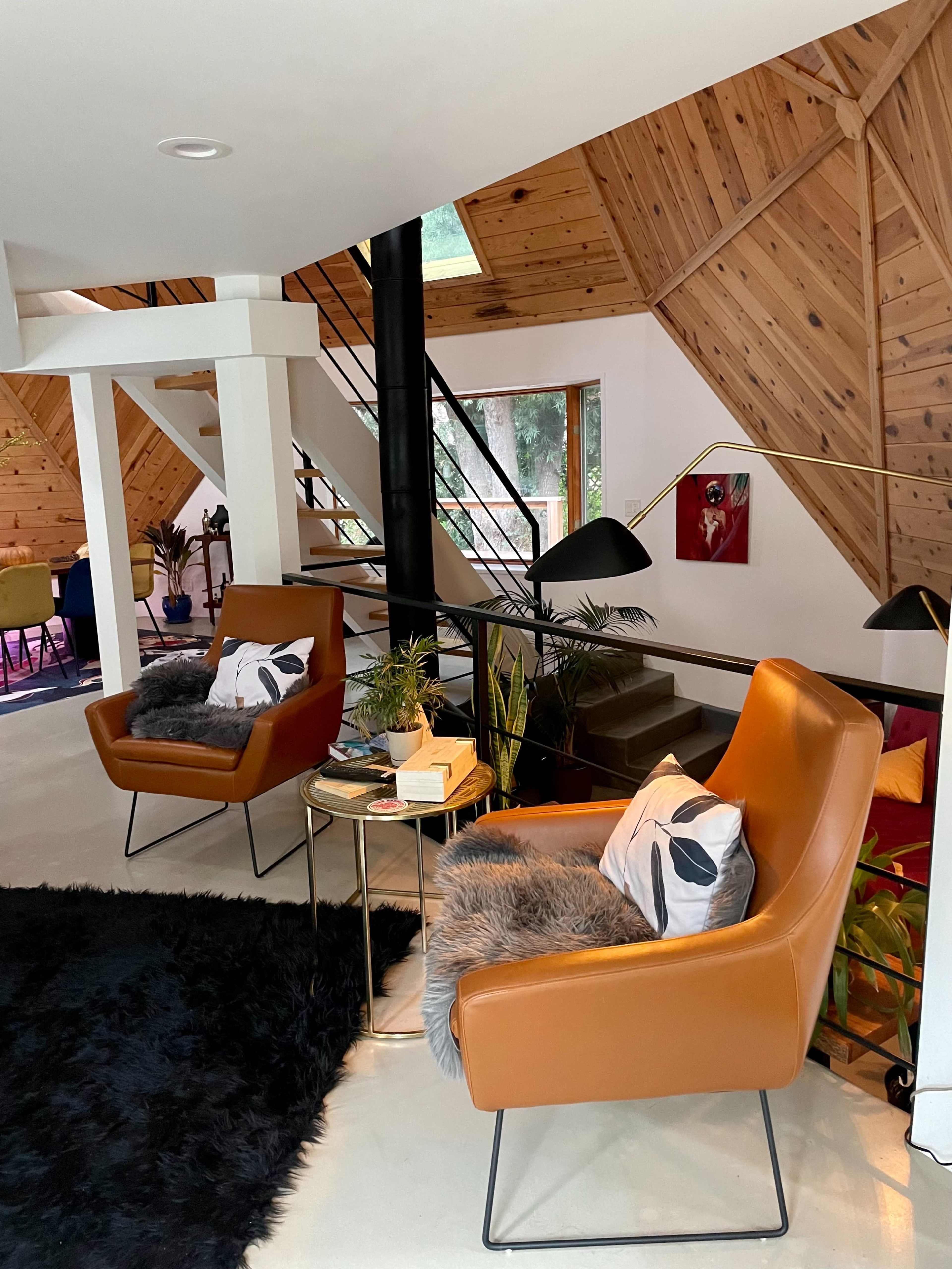 A modern living space featuring two brown chairs with pillows, a small table, and a black rug, all within a wooden interior.