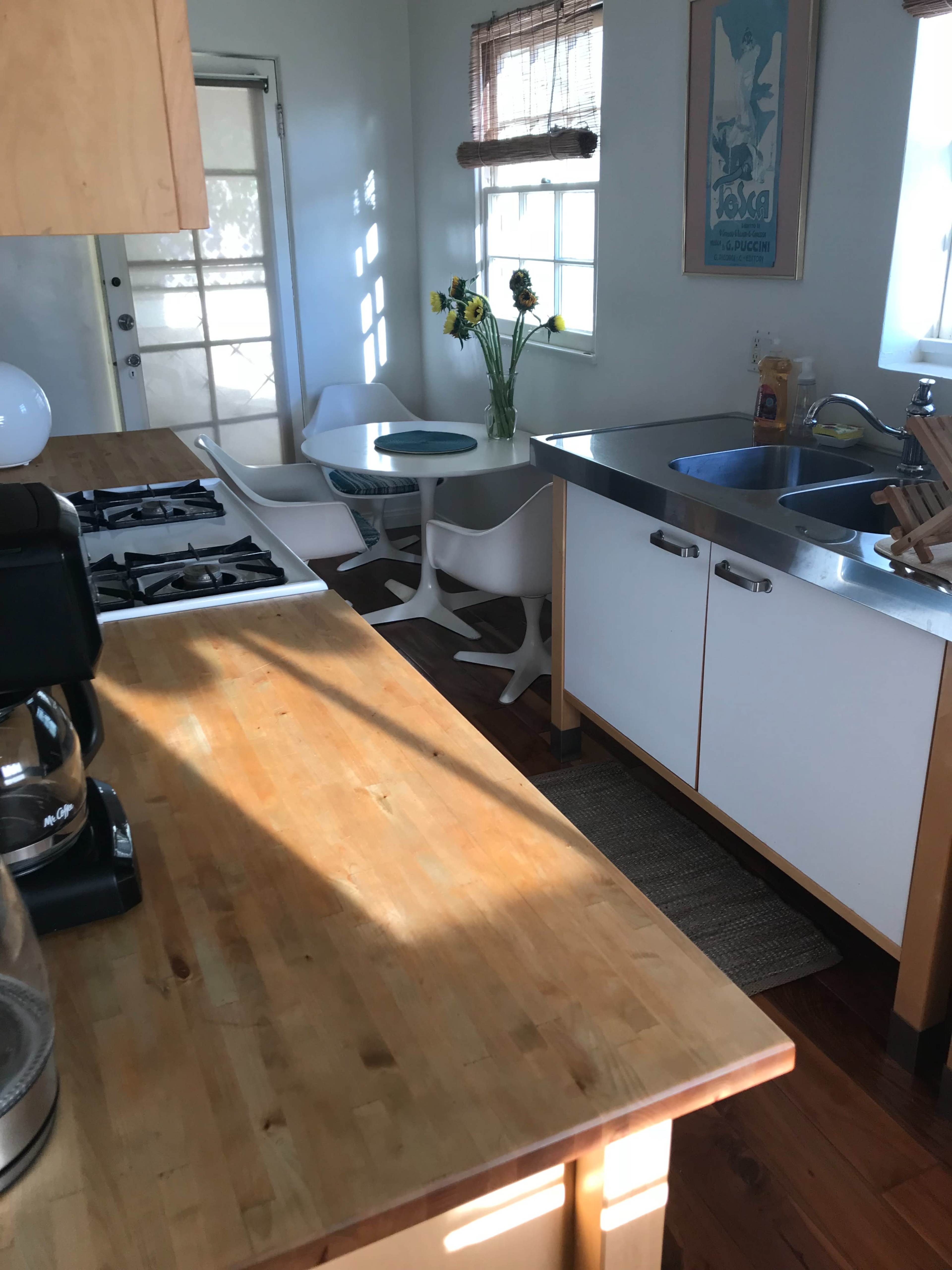 A bright kitchen with a wooden countertop, a gas stove, a modern dining table with chairs, and a vase of sunflowers.