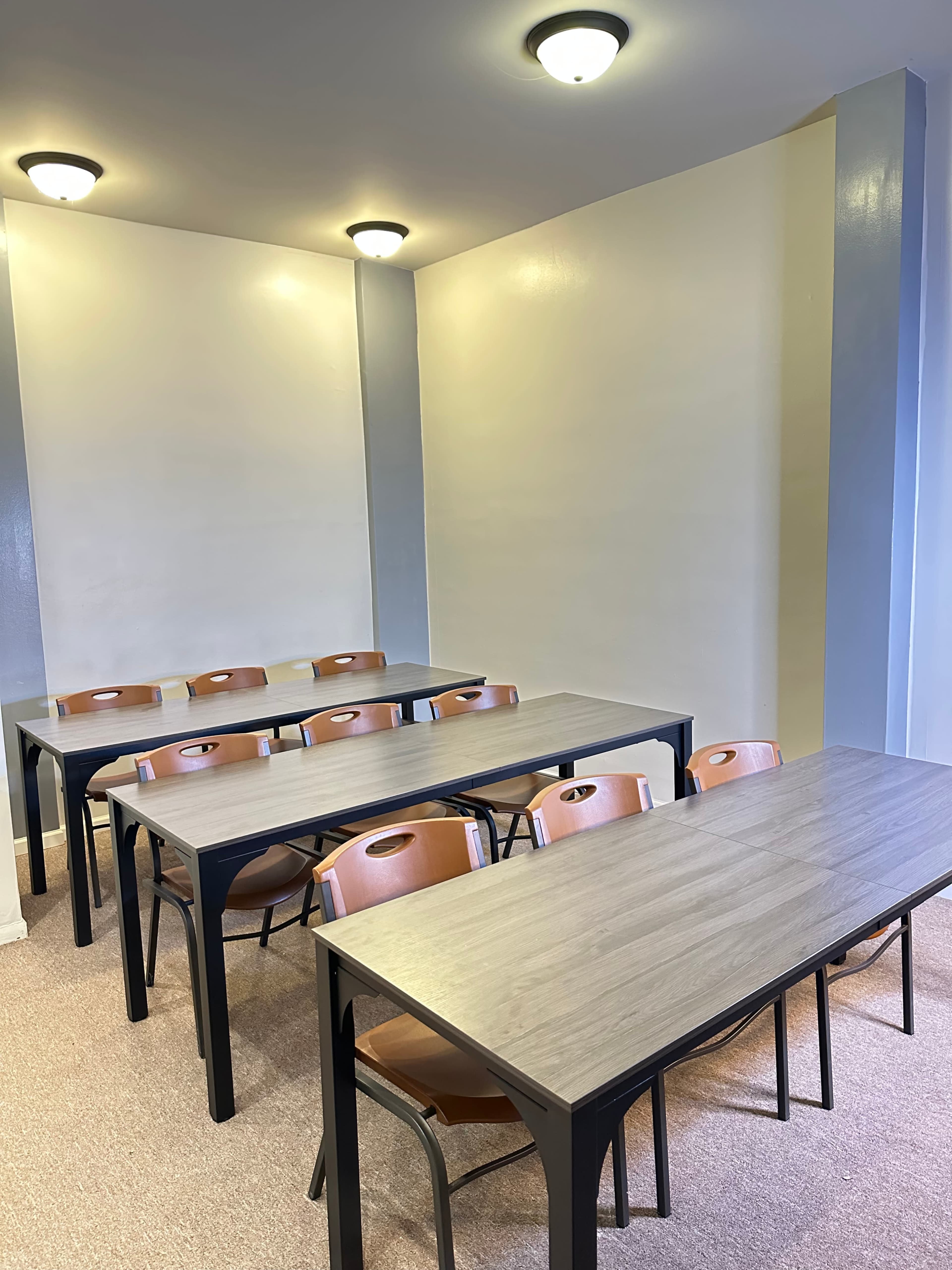 A classroom features multiple tables arranged in rows with chairs, and the walls are painted a light color.