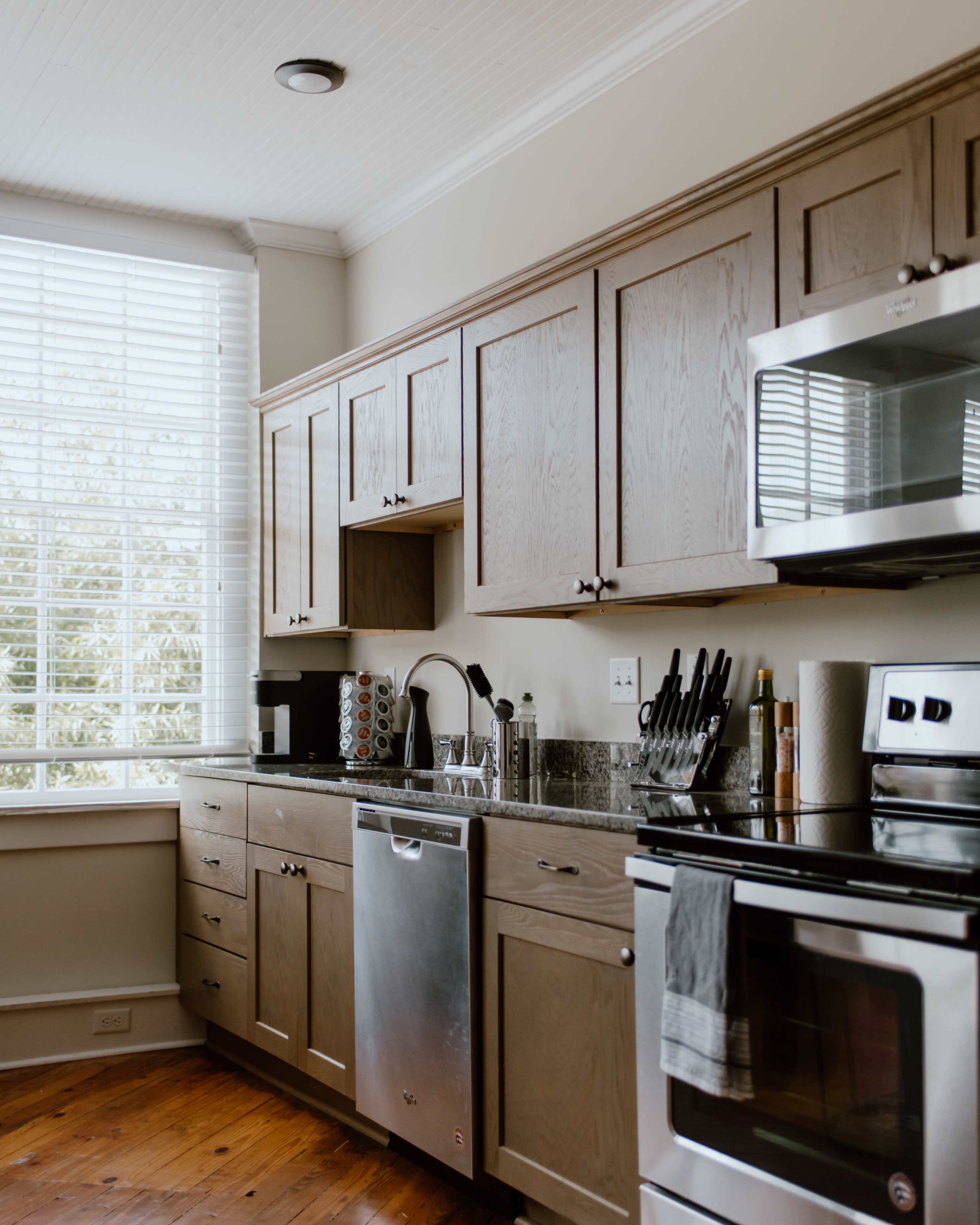 A modern kitchen with wooden cabinets, stainless steel appliances, and a large window allowing natural light to enter.
