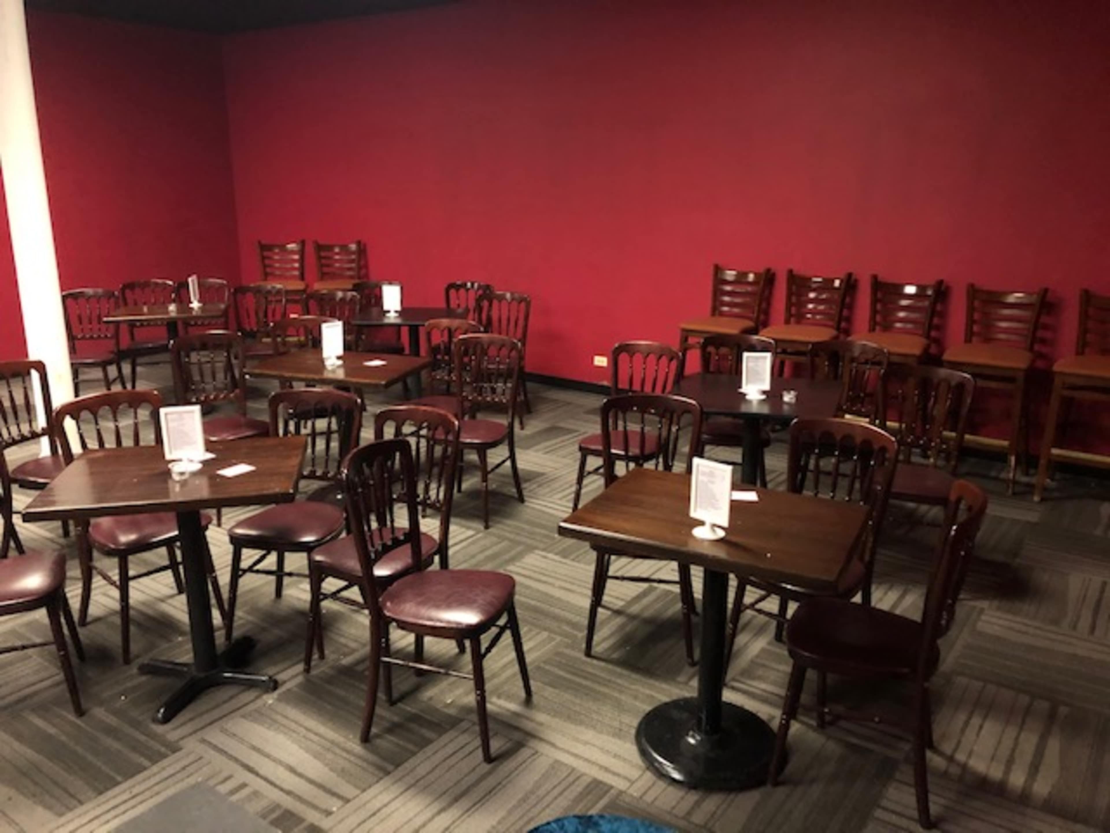 A dining area with several dark wooden tables and chairs arranged neatly against a red wall.