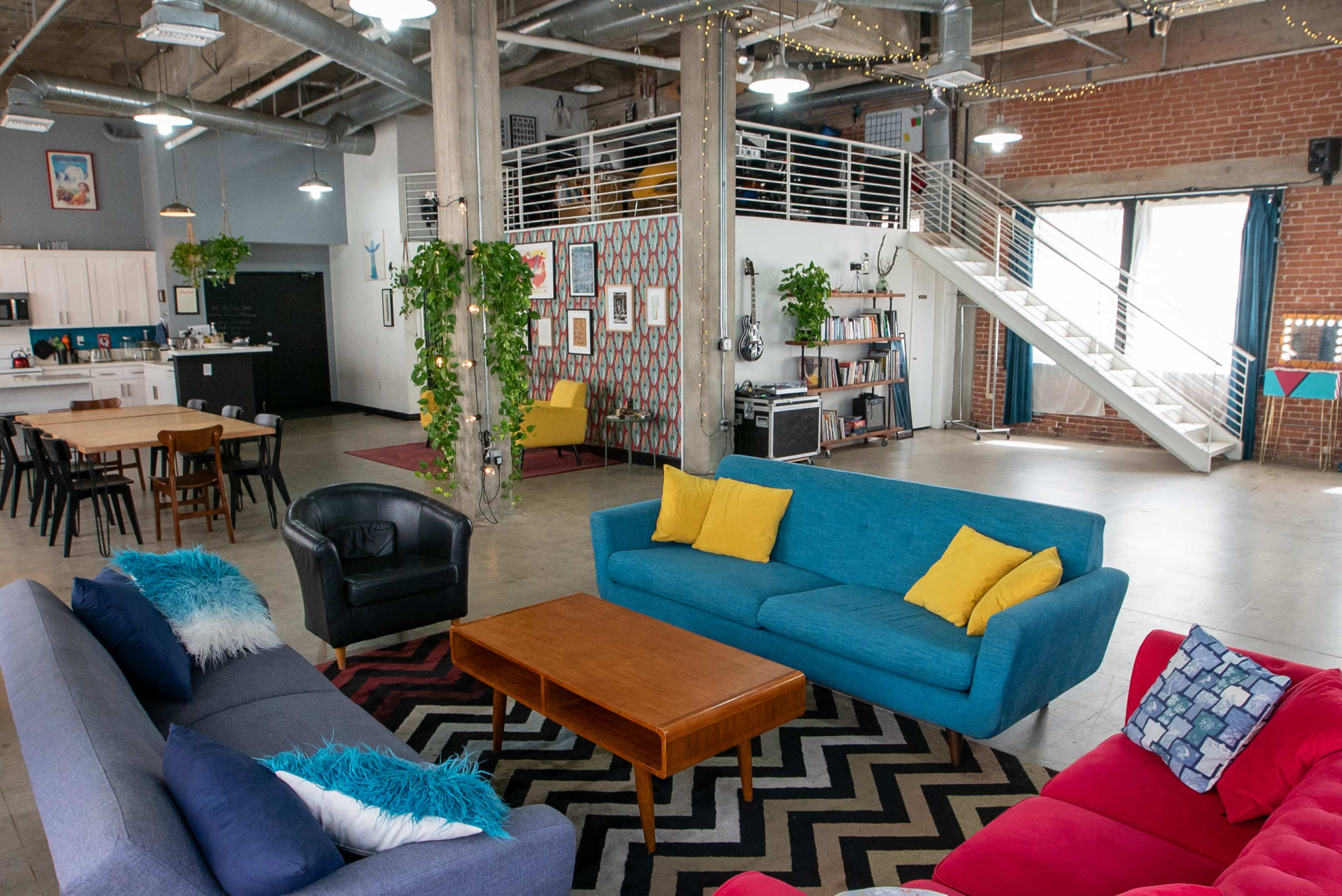 A spacious, modern communal area features colorful couches, a wooden coffee table, and a kitchen in the background.