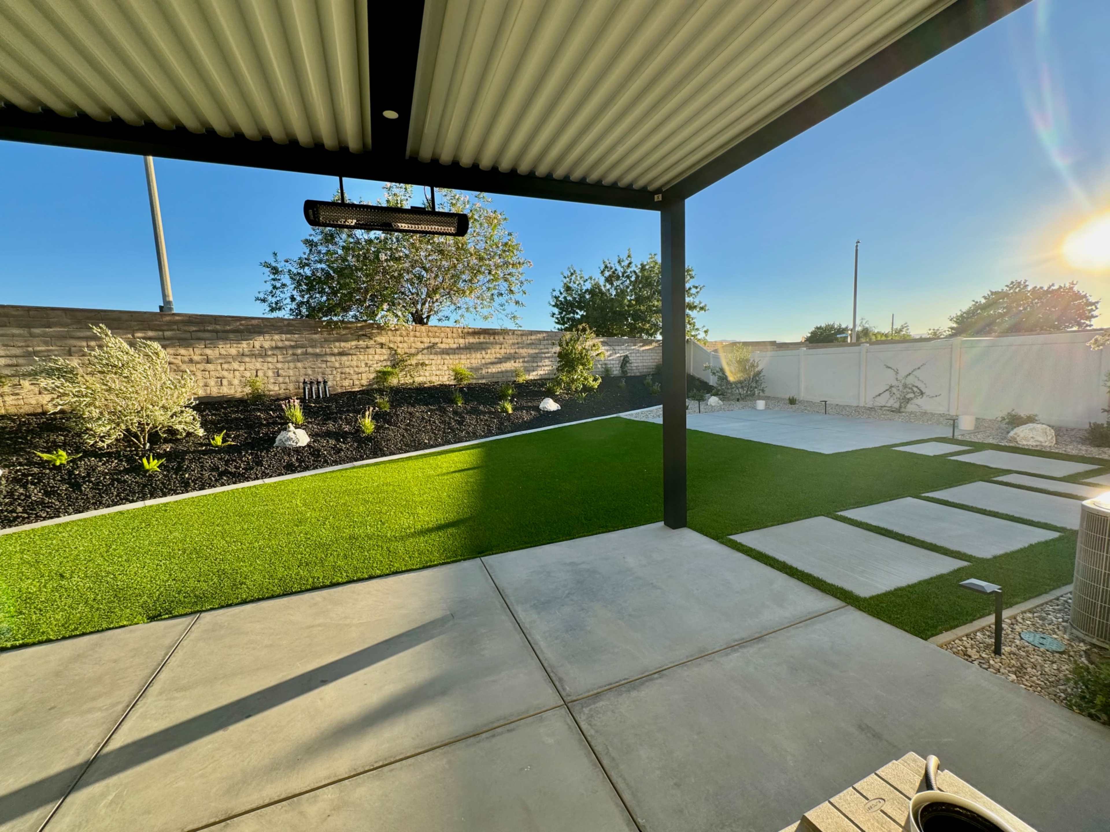 A well-maintained backyard with artificial turf, concrete pathways, and landscaped areas featuring plants and decorative stones.