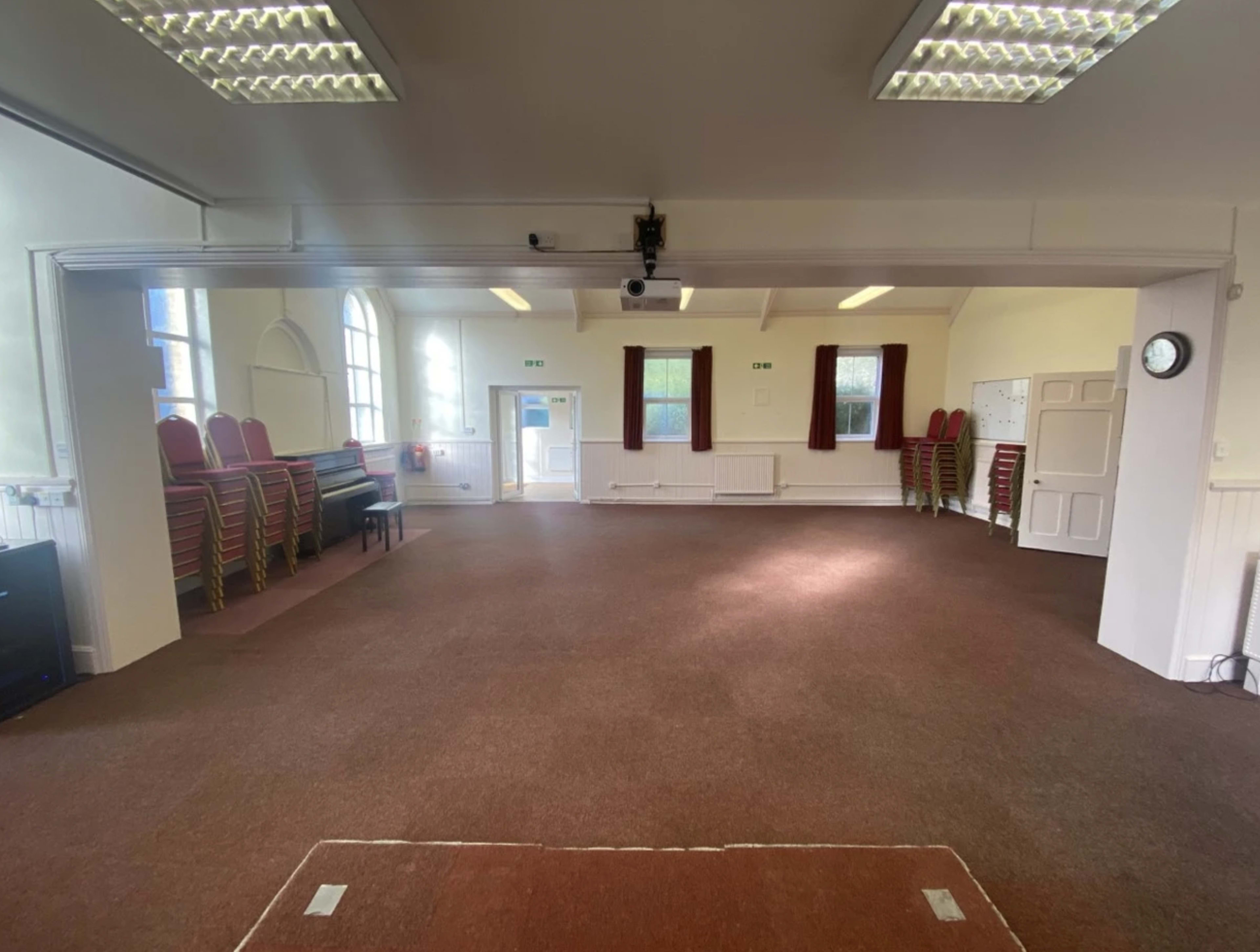 A spacious room with a carpeted floor, chairs stacked against one wall, and a door leading to the outside.