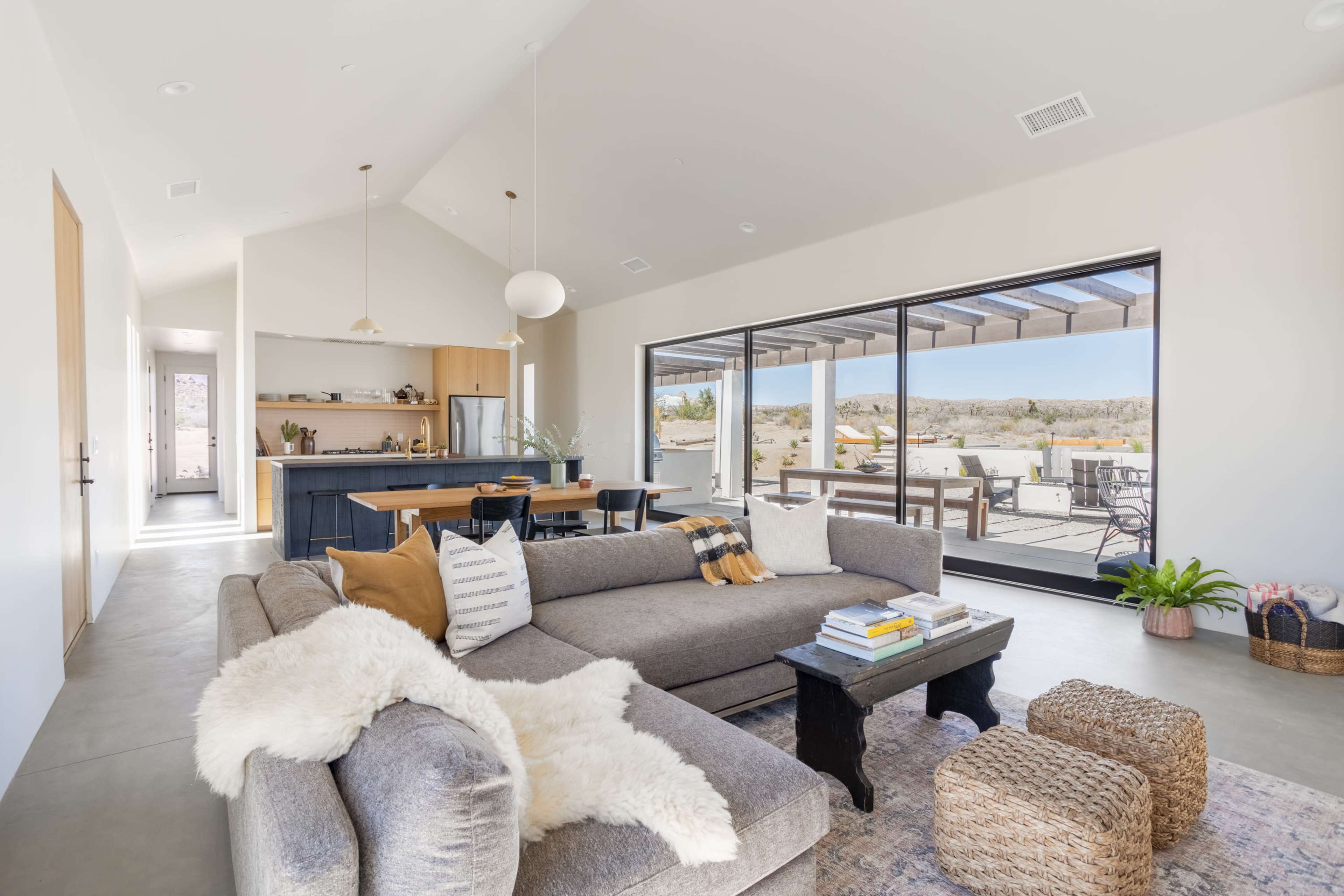 A modern living room with a gray sectional sofa, a coffee table, and a view of an outdoor patio through large glass doors.