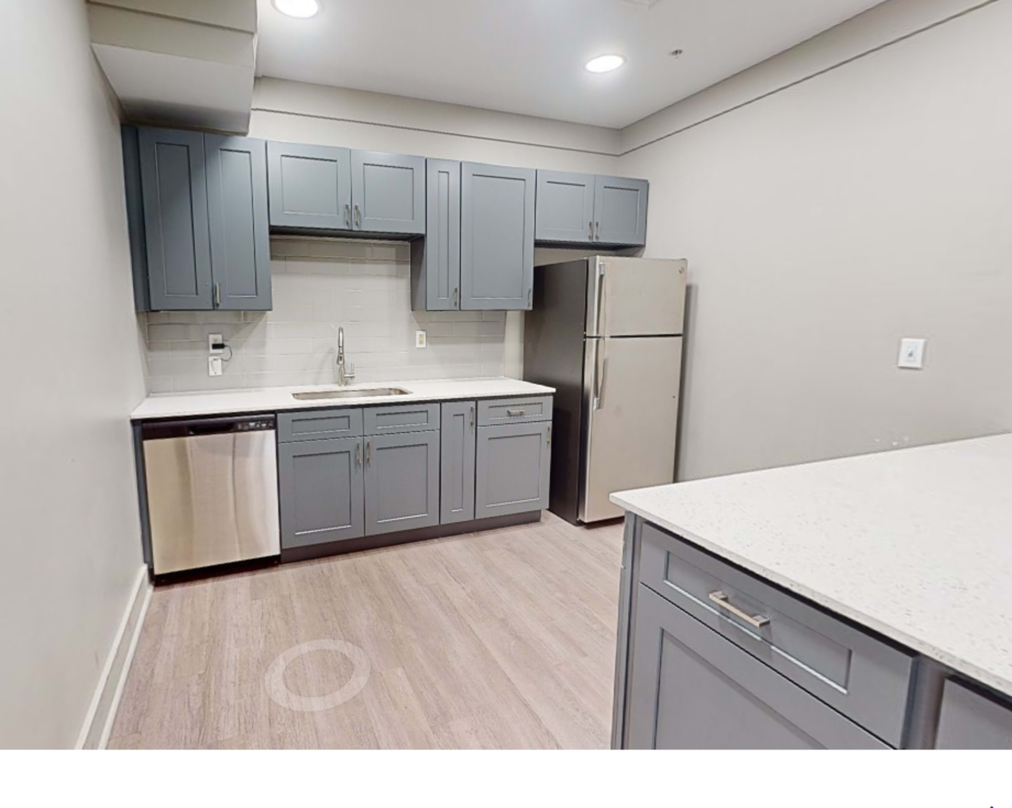 A modern kitchen with gray cabinetry, stainless steel appliances, and a light-colored countertop.