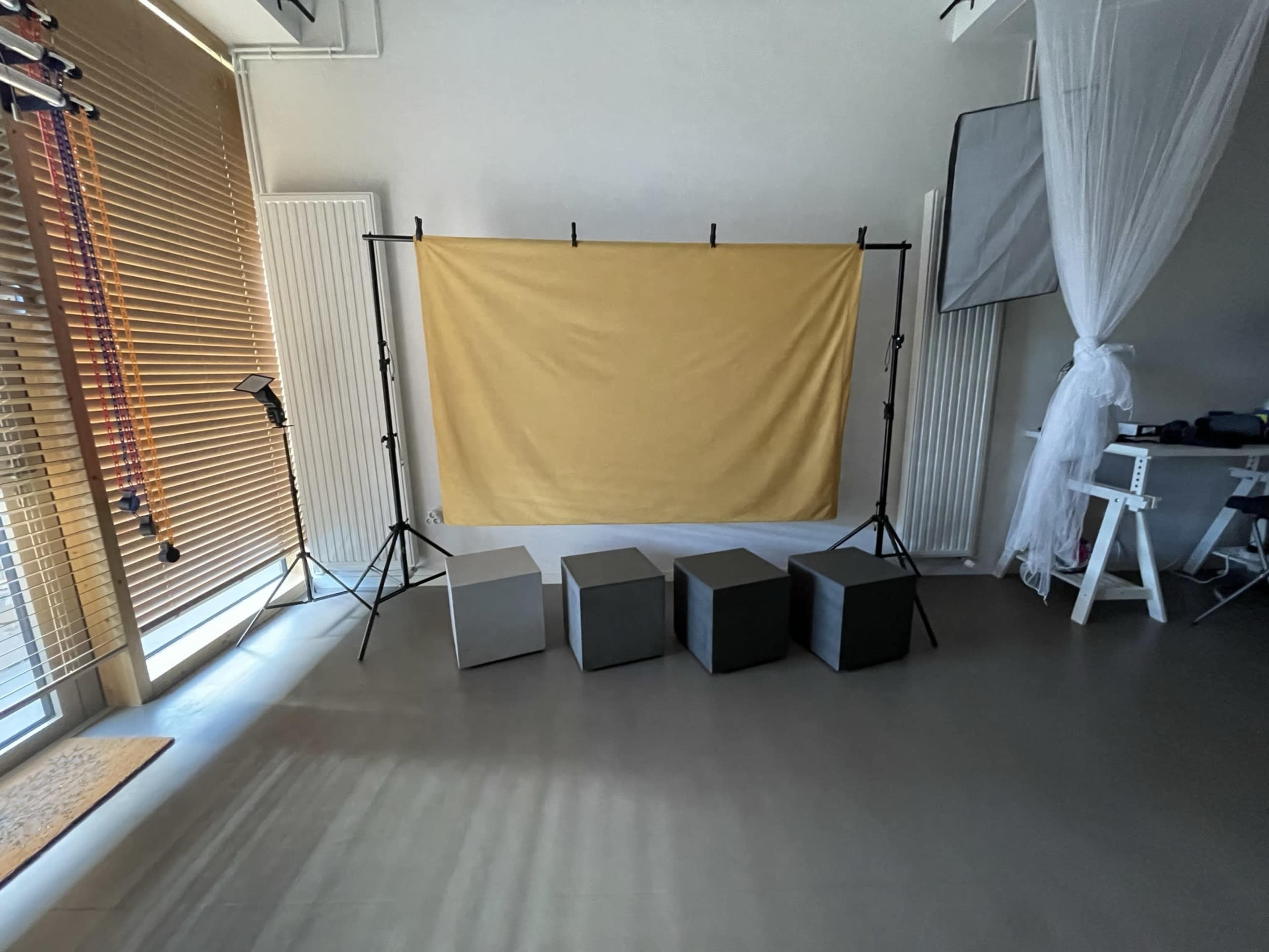 A photography setup featuring a yellow backdrop supported by stands, with four square stools arranged in front on a smooth floor.