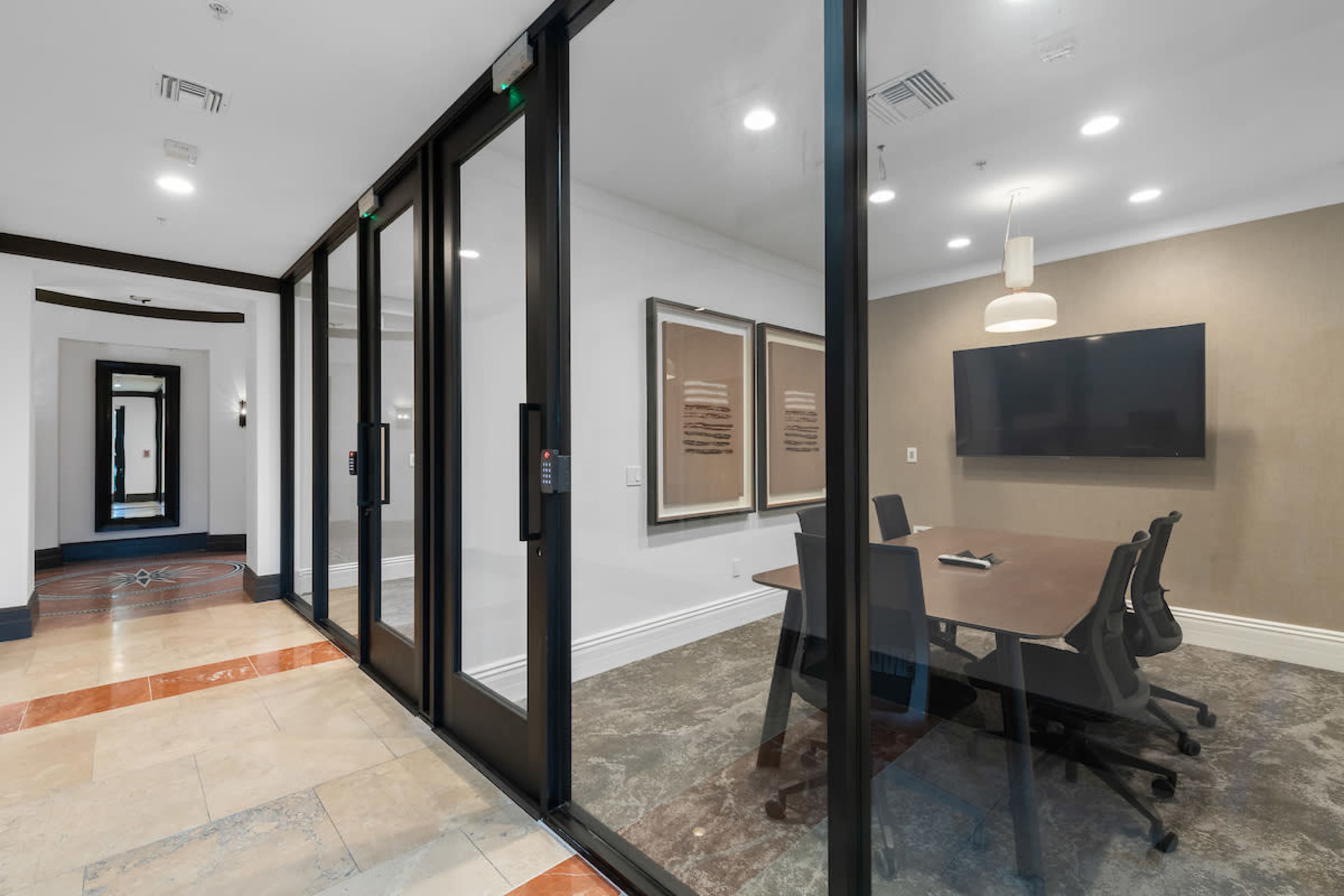 A modern conference room with glass walls, a large table, black chairs, and a flat-screen monitor.