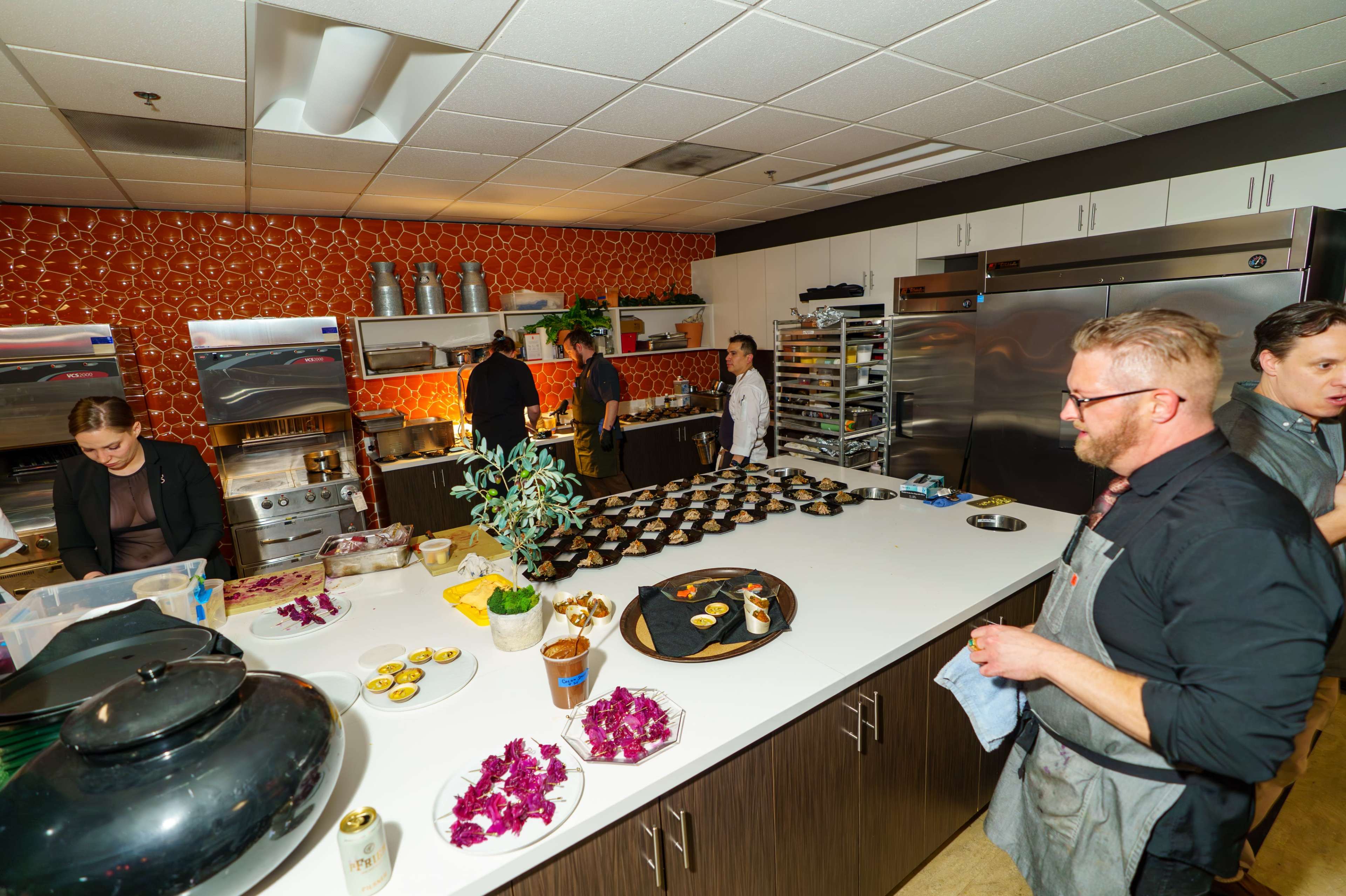 A modern kitchen is bustling with chefs preparing a variety of dishes on a large countertop, while others work in the background.