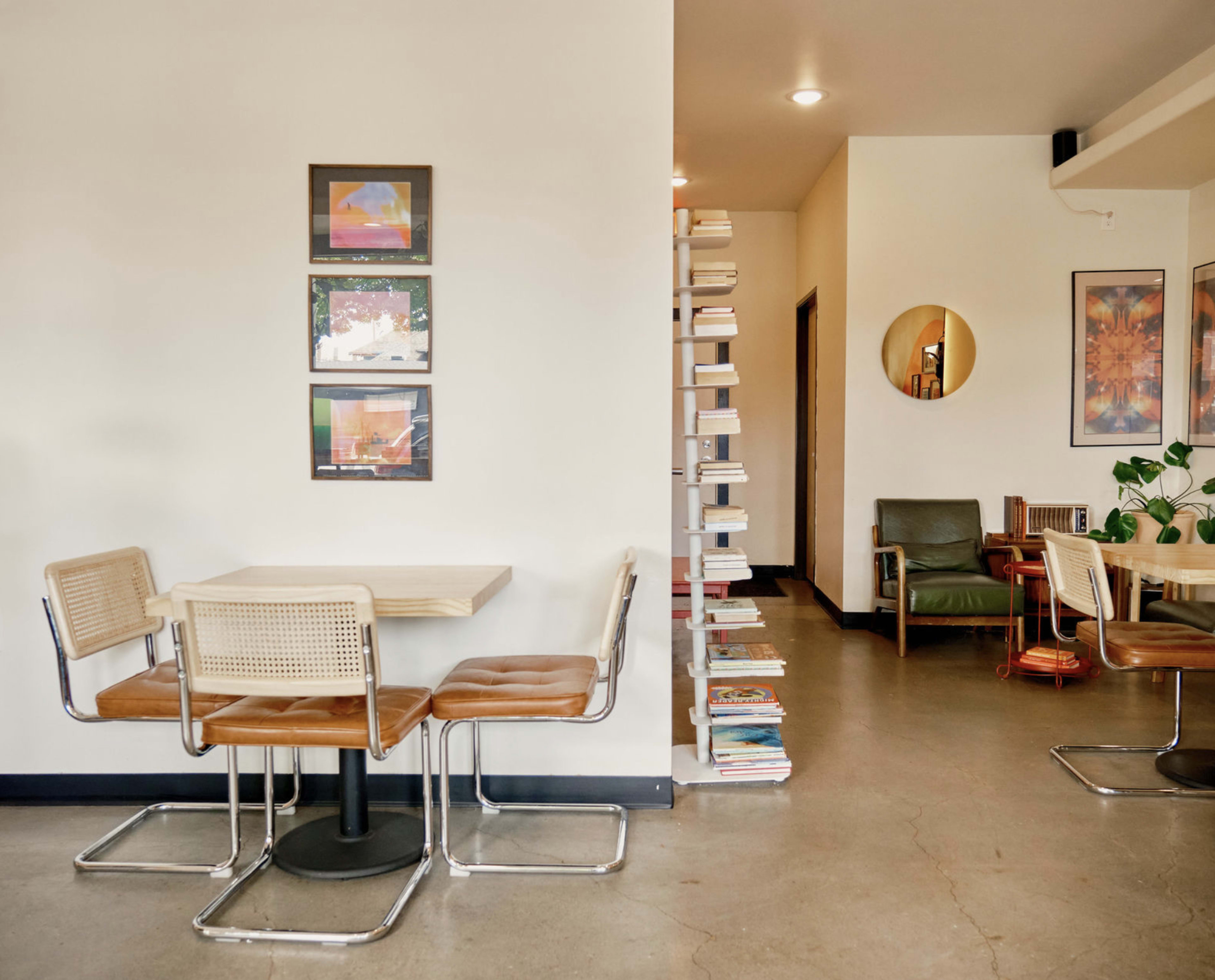 The image shows a cozy café interior with a wooden table and metal chairs on one side, while a book-filled wall shelf adds a decorative element to the space.