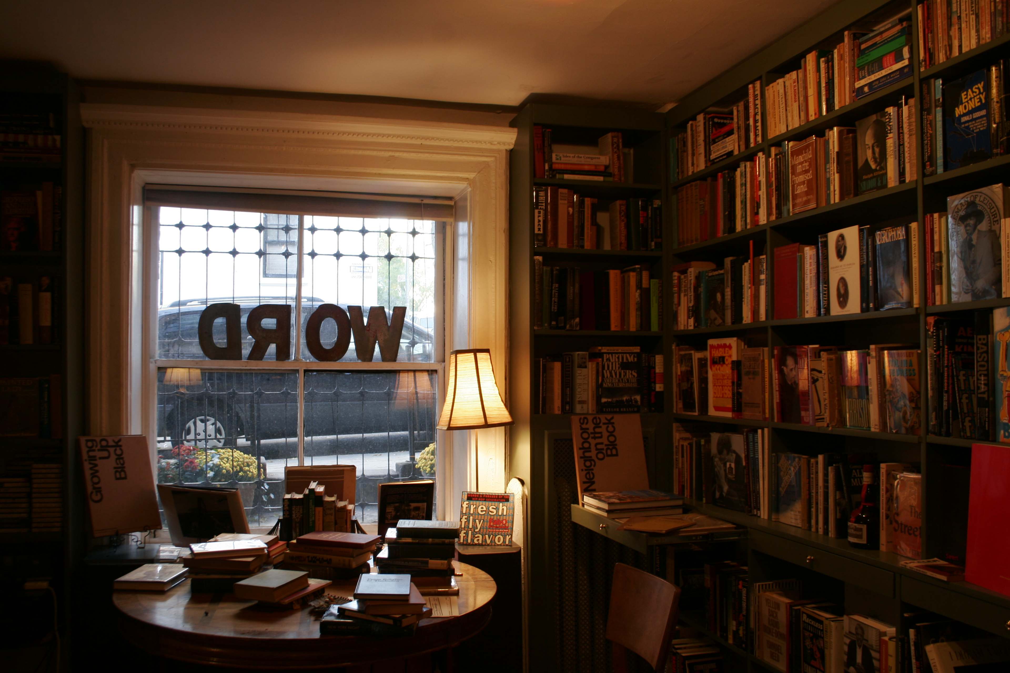 A cozy bookstore interior features bookshelves filled with various books, a table in the center, and large windows with the word "WORD" displayed prominently.