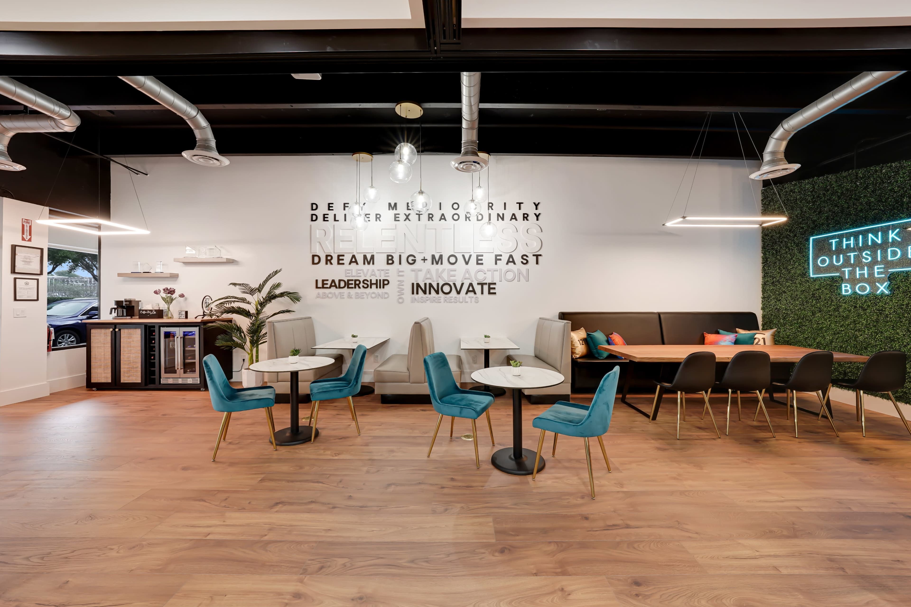 A modern coworking space with circular tables and teal chairs, a booth area, and motivational text on the walls.