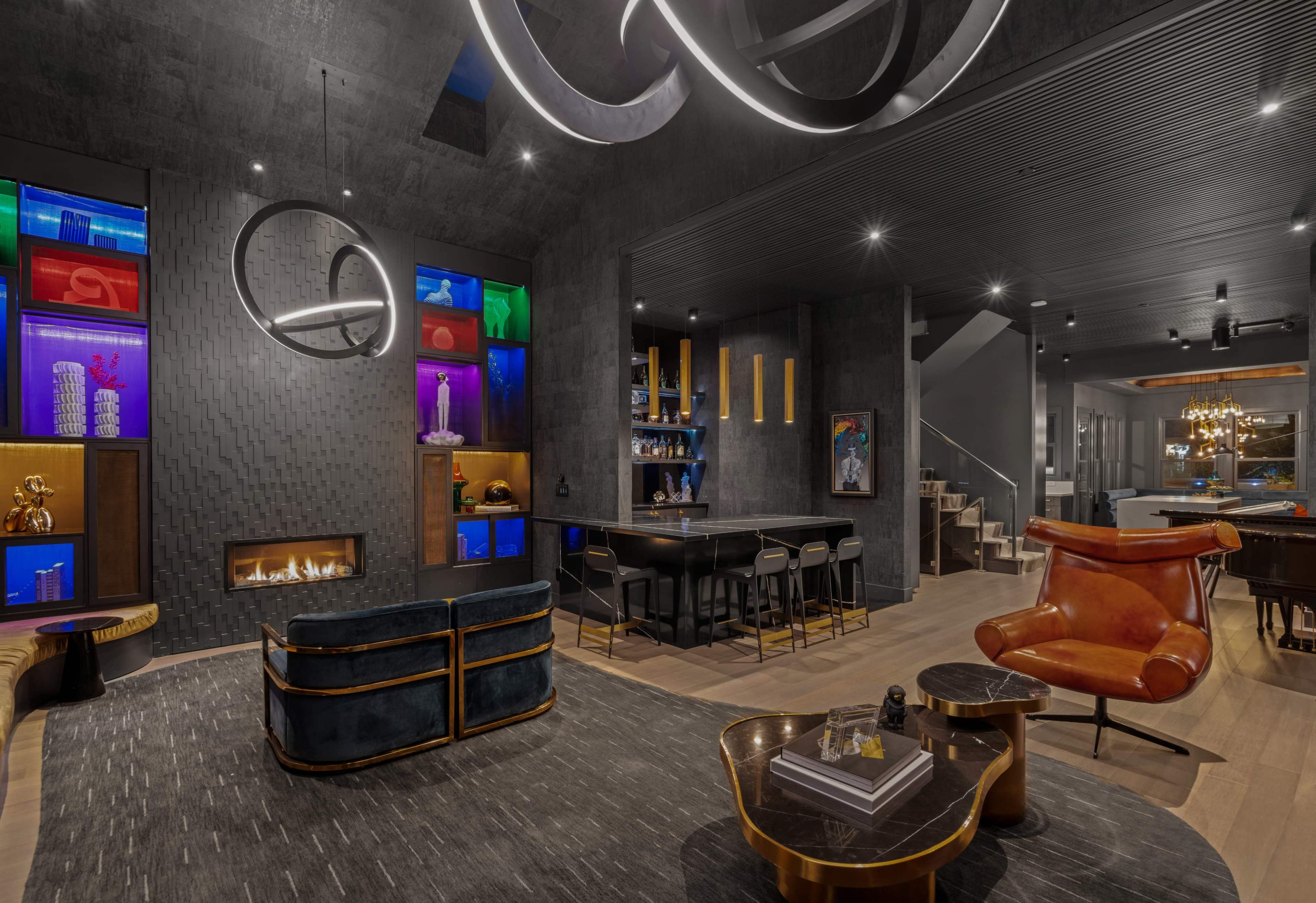 A modern interior space with a fireplace, a bar area, and colorful illuminated displays set against a dark wall, furnished with stylish seating and a geometric rug.