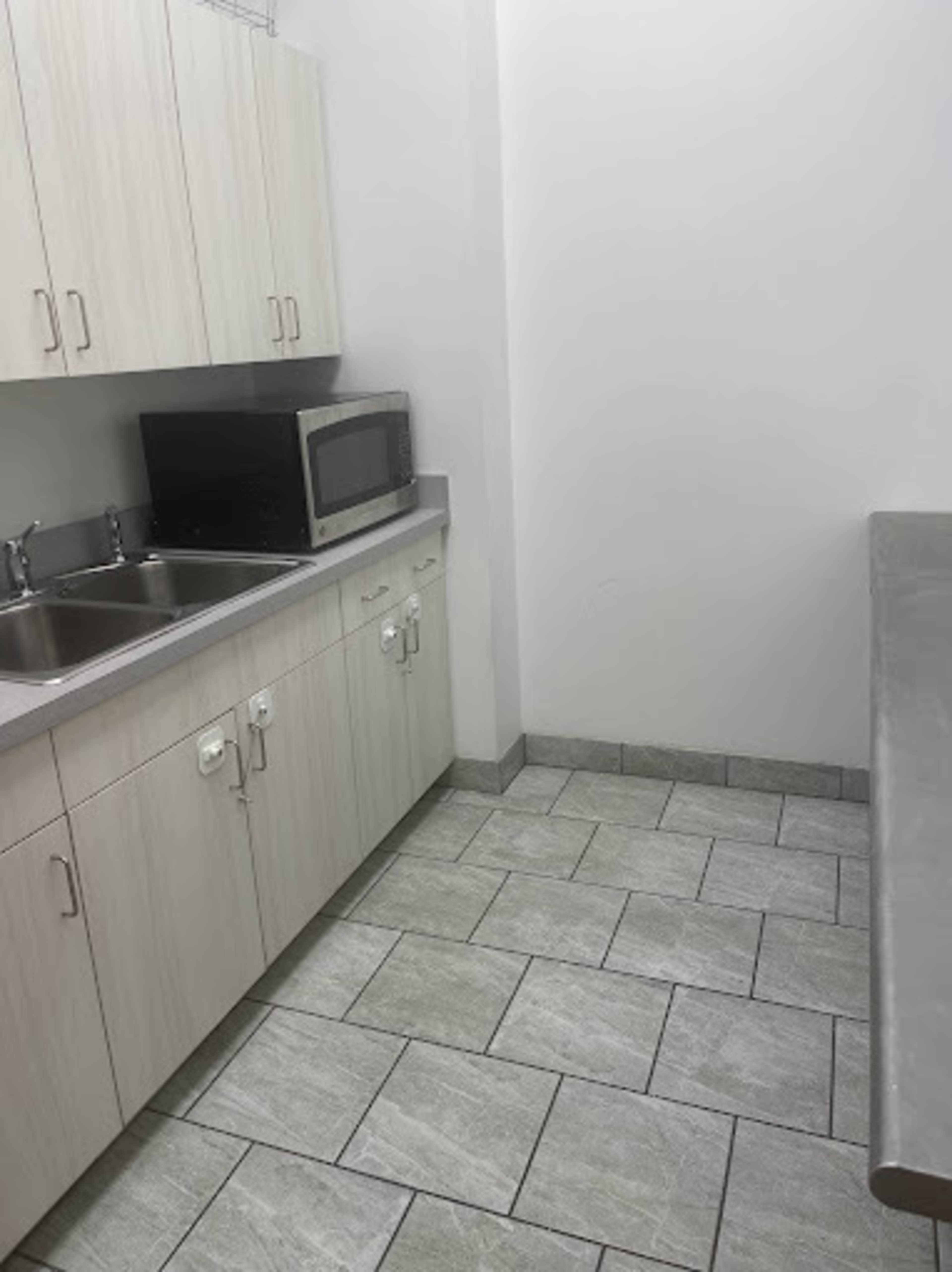 The image shows a small kitchen area with a double sink, a microwave on a countertop, and tiled flooring.