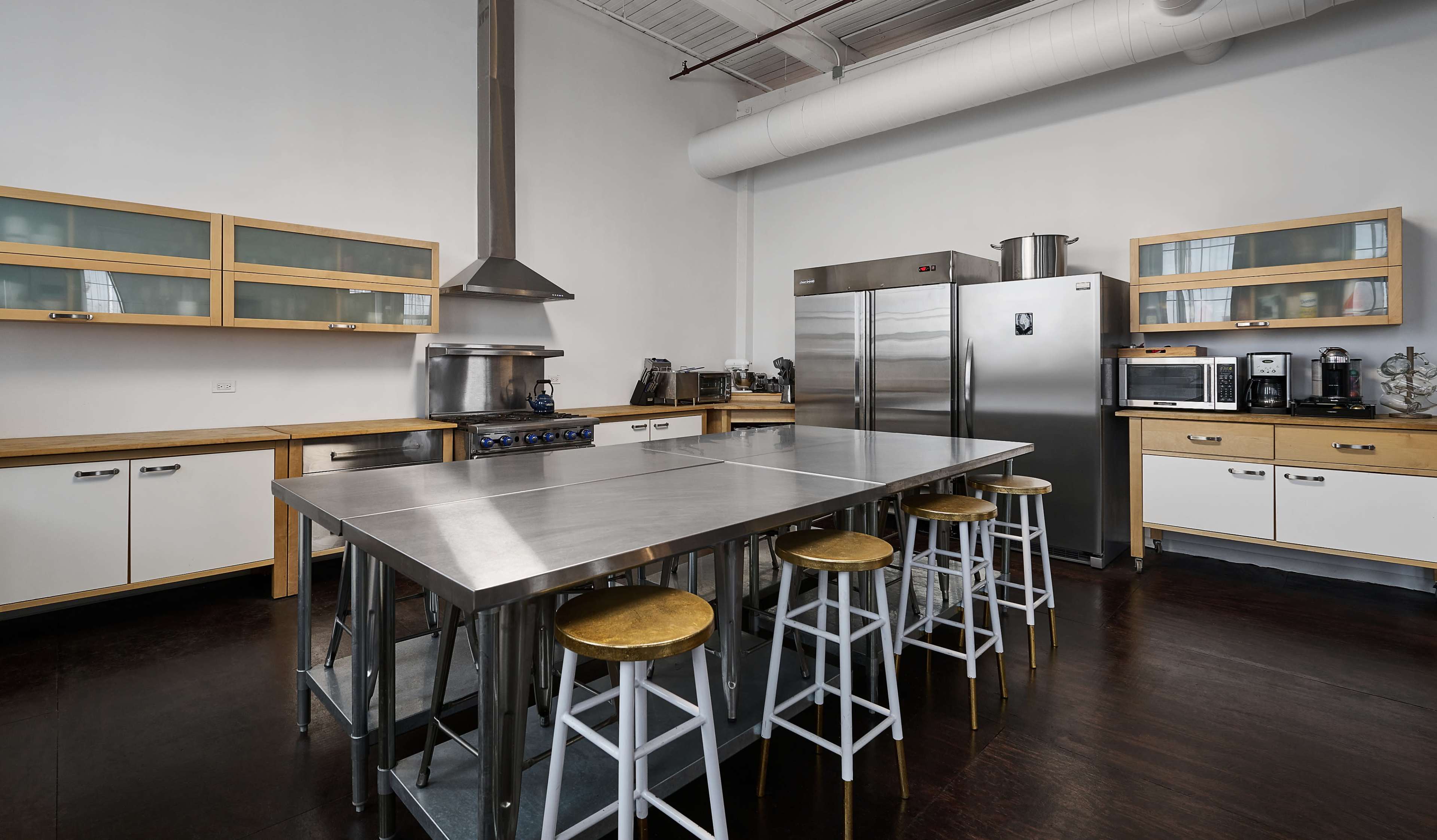 The image shows a modern kitchen with stainless steel countertops, wooden cabinets, and various kitchen appliances.