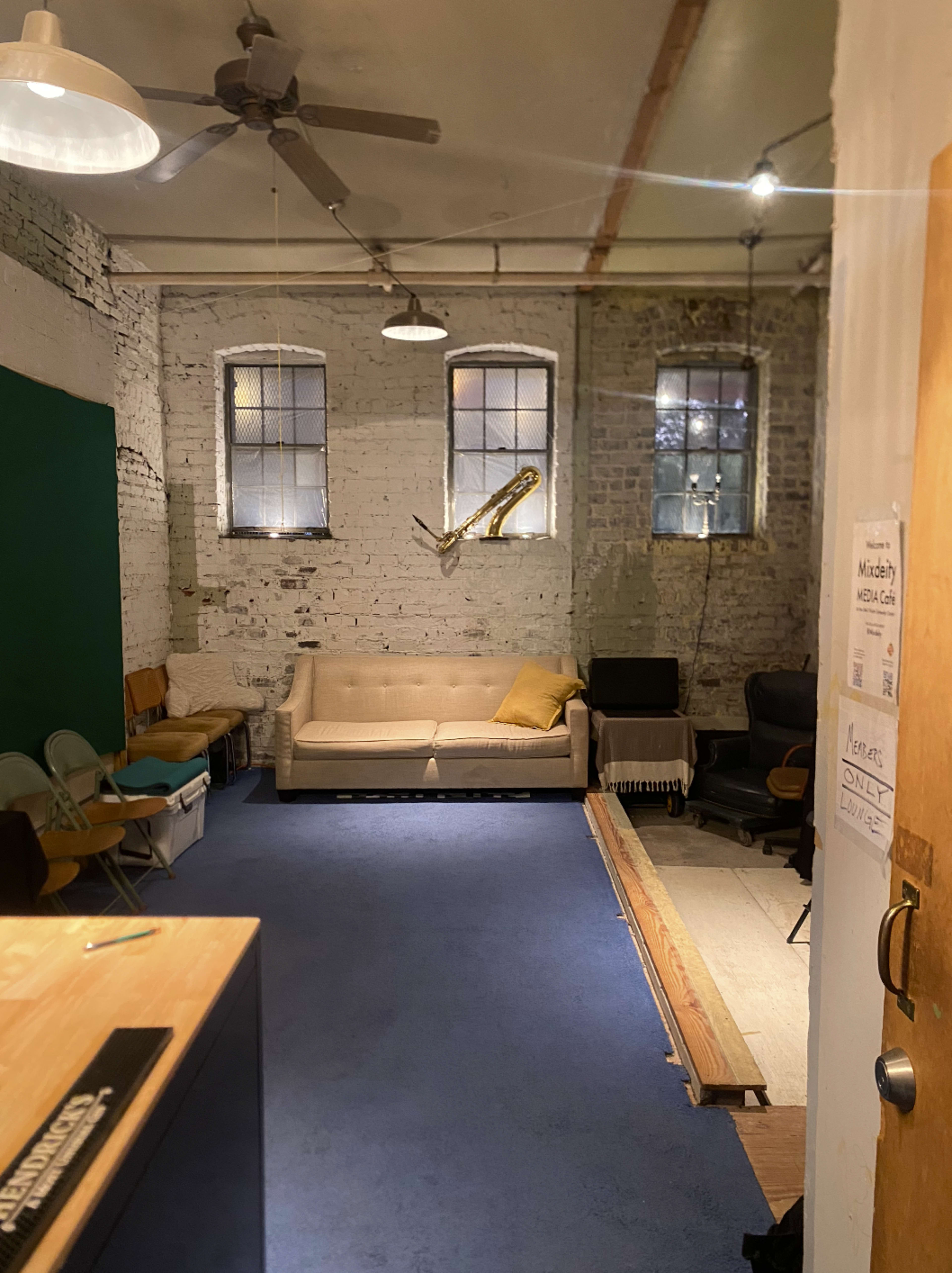 An interior room with exposed brick walls, a beige sofa, two windows, and a wooden door on the right.