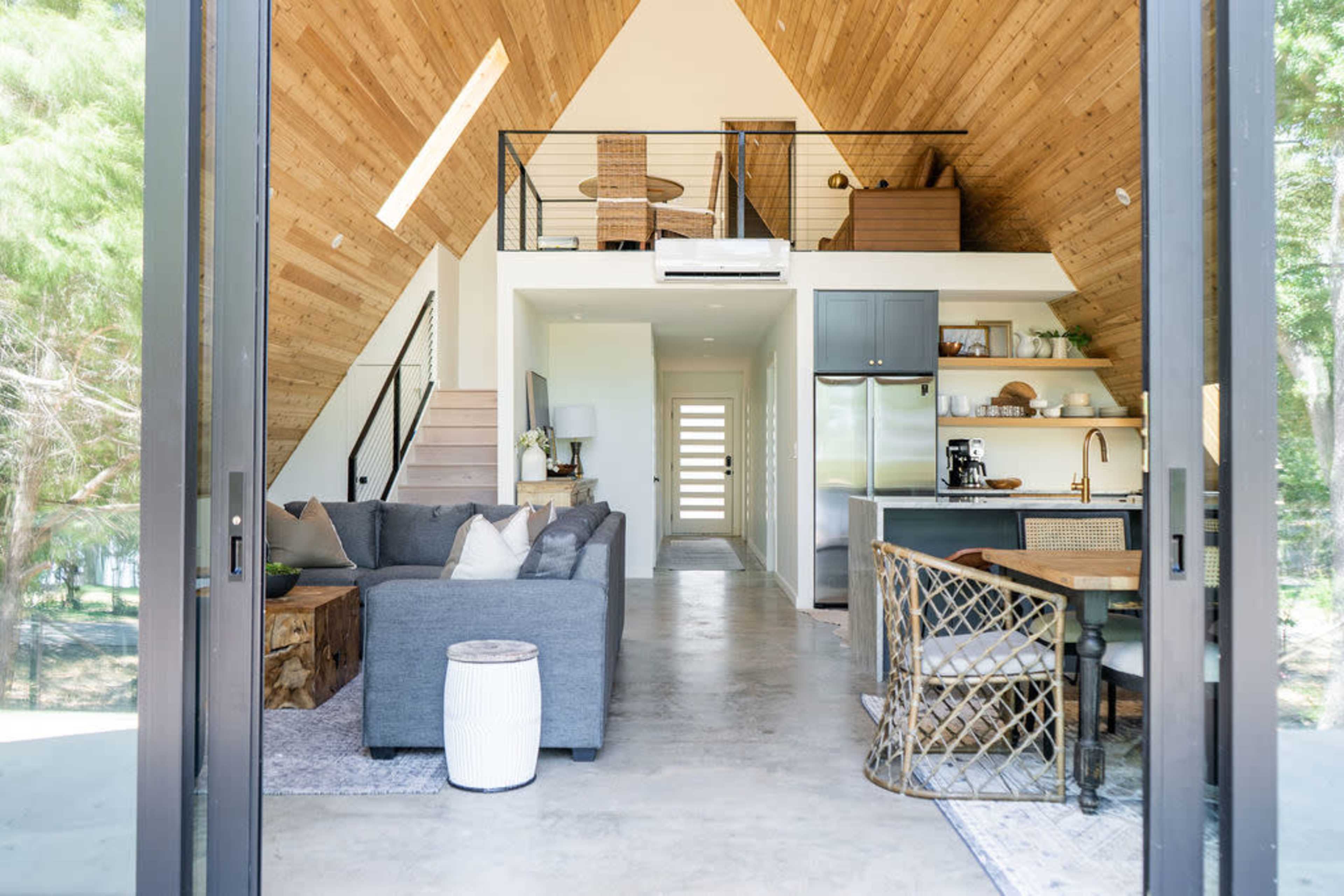 A modern, open-concept living space with high wooden ceilings, a kitchen area, a dining table, and a cozy seating area.