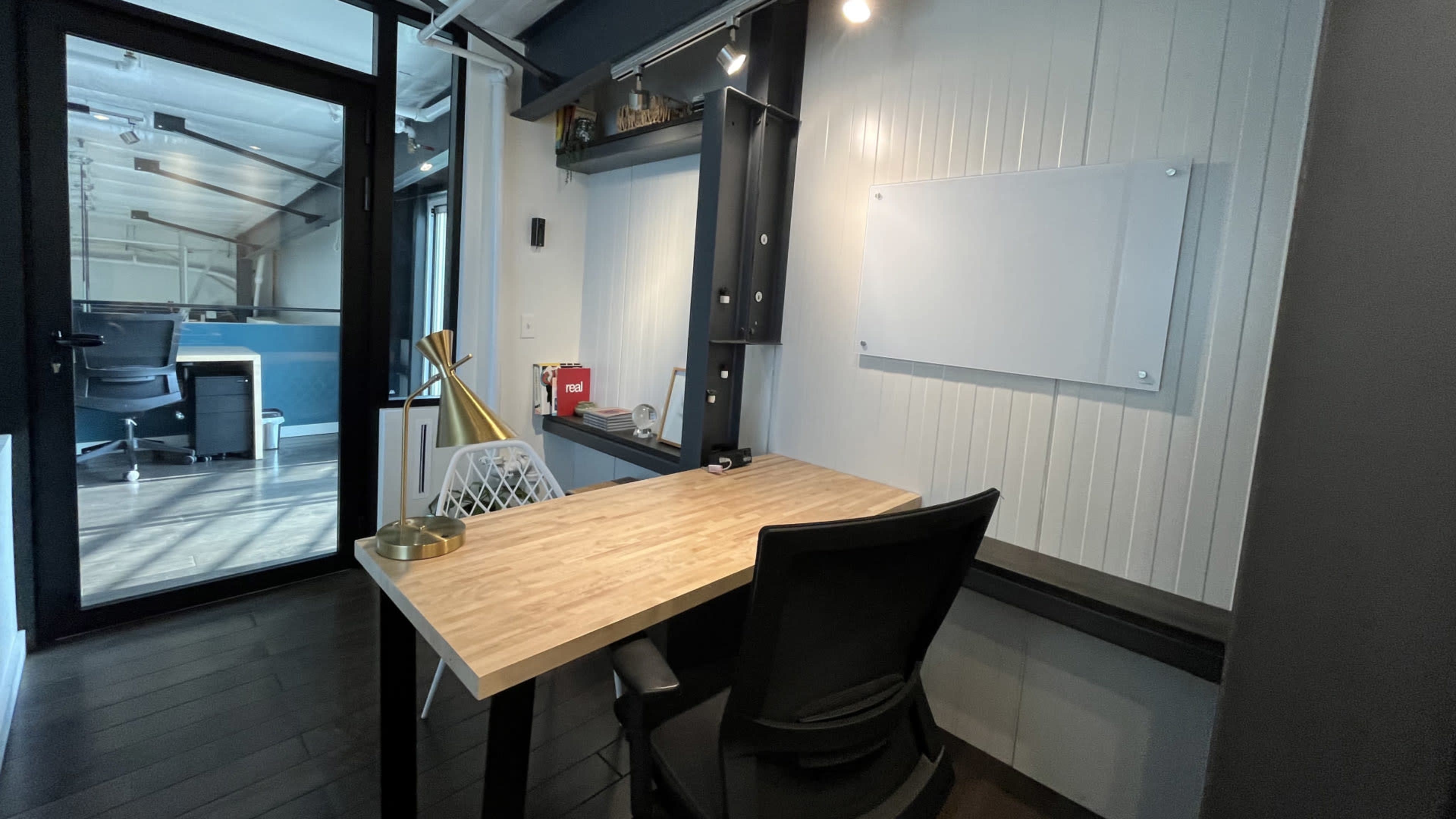 A modern office space with a wooden desk, a black office chair, and a whiteboard mounted on the wall.