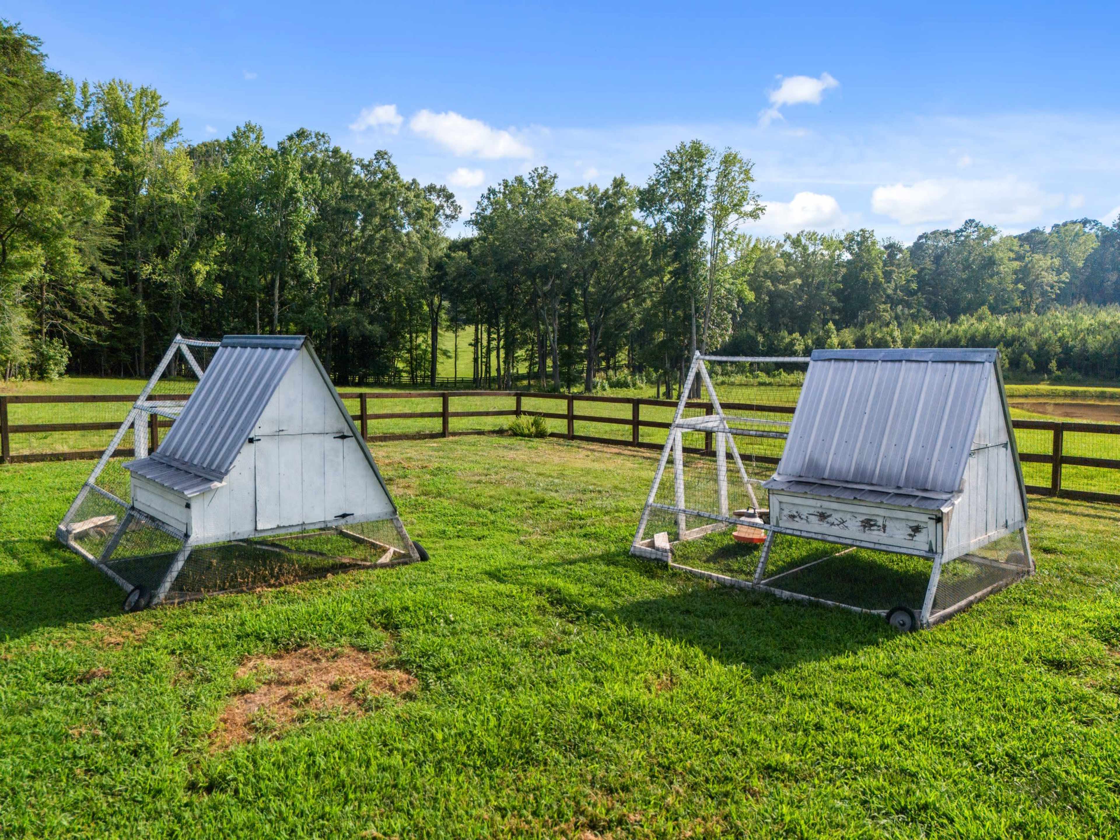 Two A-frame chicken coops are situated on a grassy field enclosed by a wooden fence.