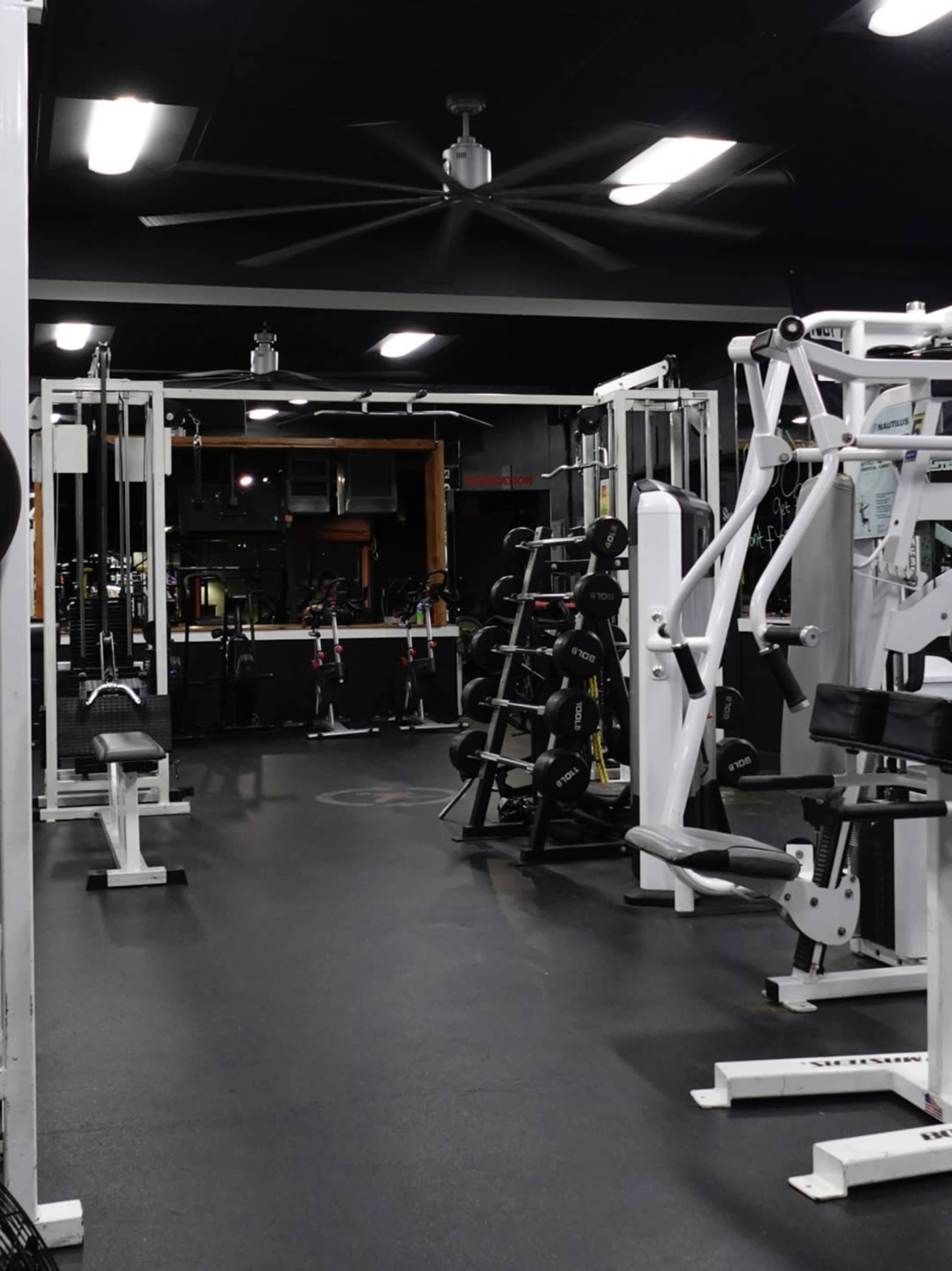 The image shows a fitness gym featuring various weightlifting machines and free weights arranged in a spacious indoor area.