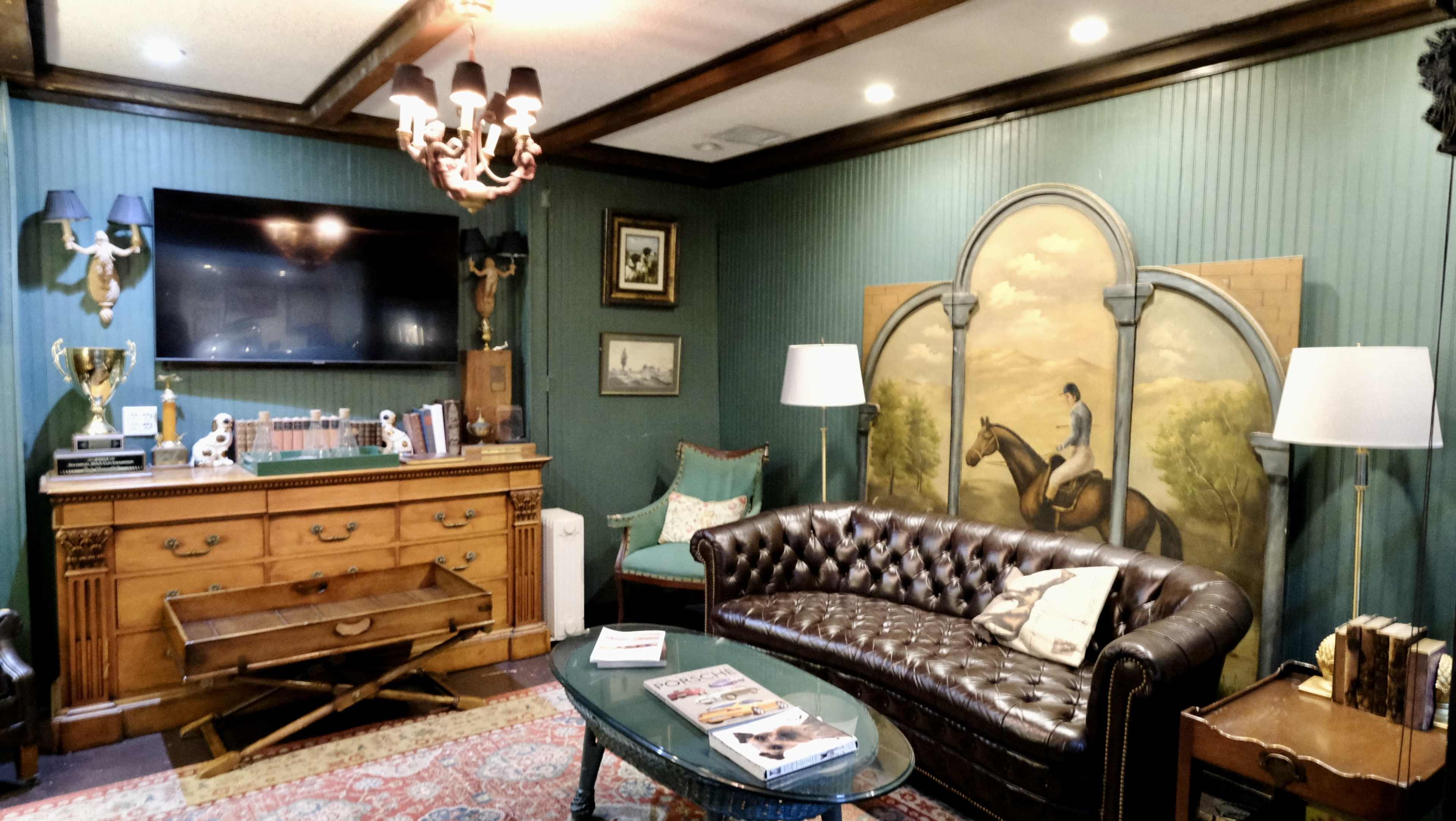 A cozy living room featuring a leather sofa, wooden furniture, a mounted television, and a large mural of a man on a horse.