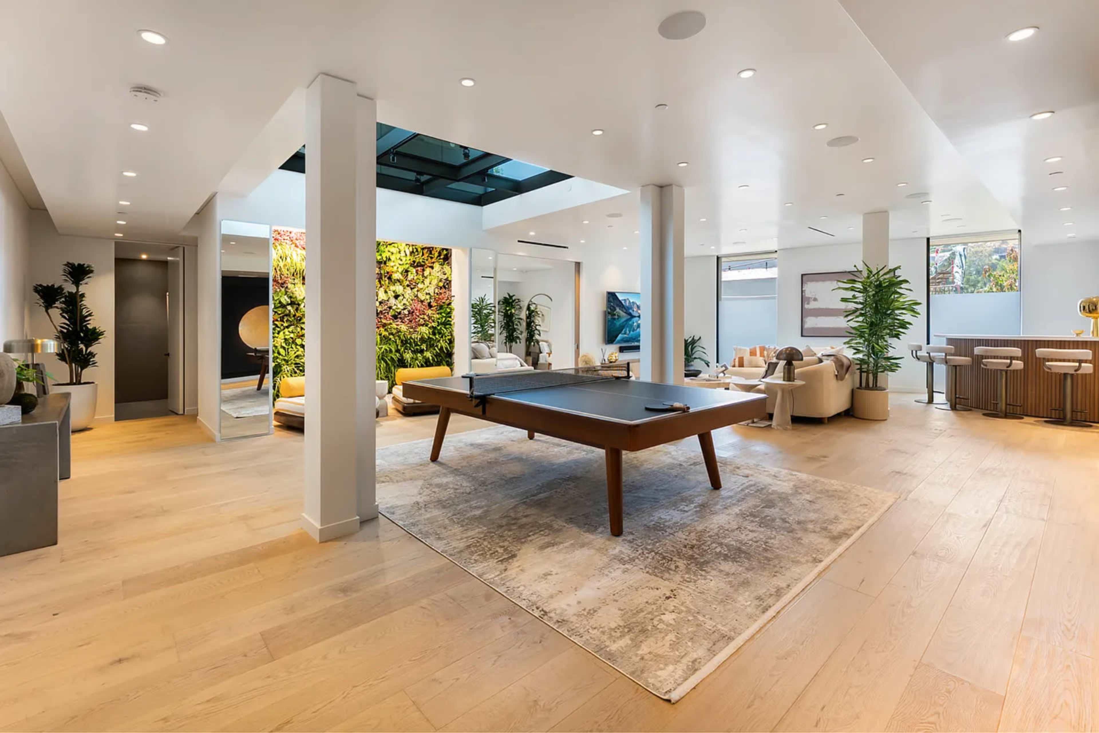 The spacious interior features a pool table in the center, surrounded by modern seating and a living wall of greenery.