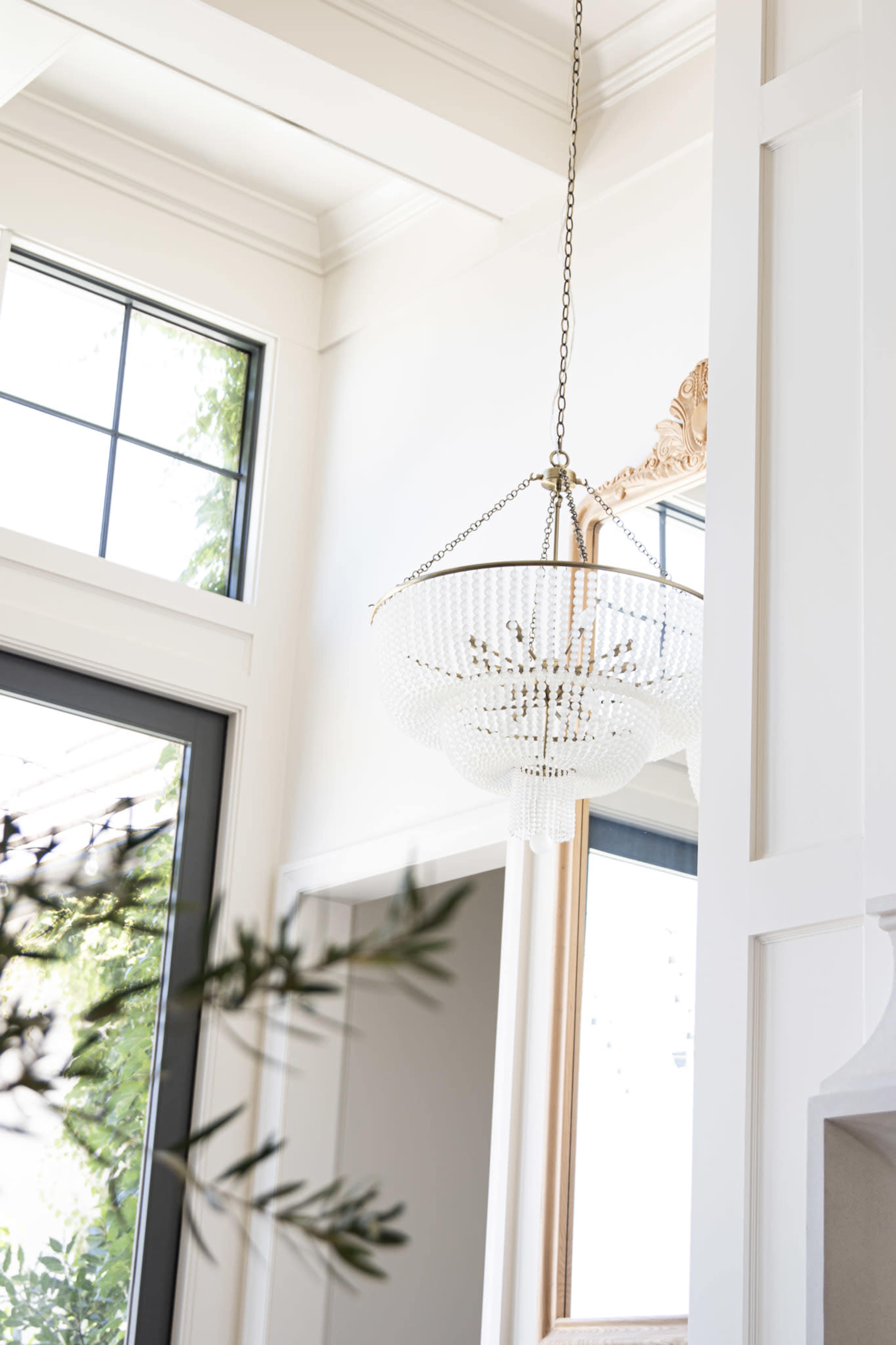 The image features a beaded chandelier hanging from a ceiling in a room with large windows and a decorative mirror.