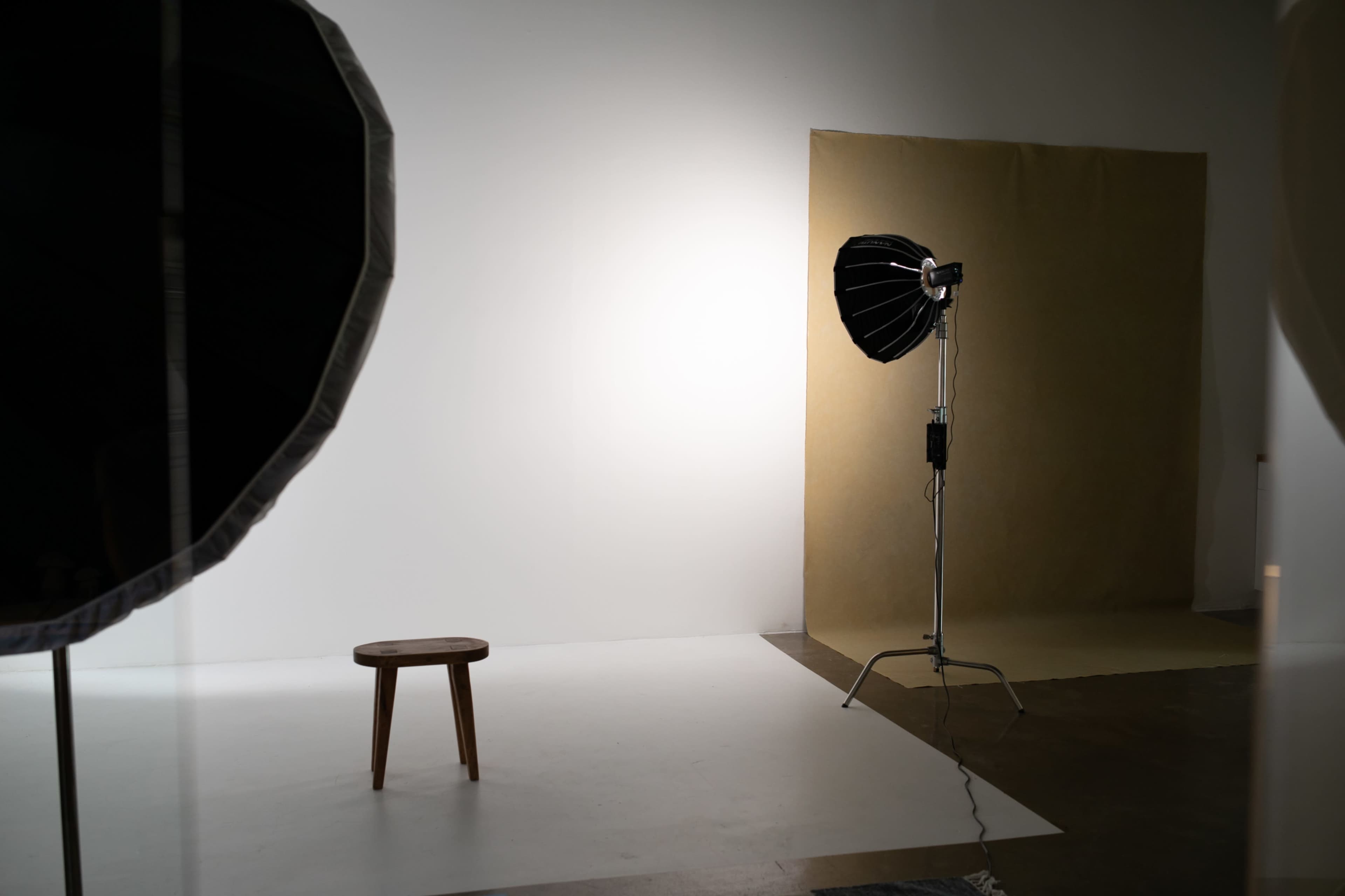 The image shows a photography studio setup featuring a wooden stool, a backdrop, and studio lighting equipment.