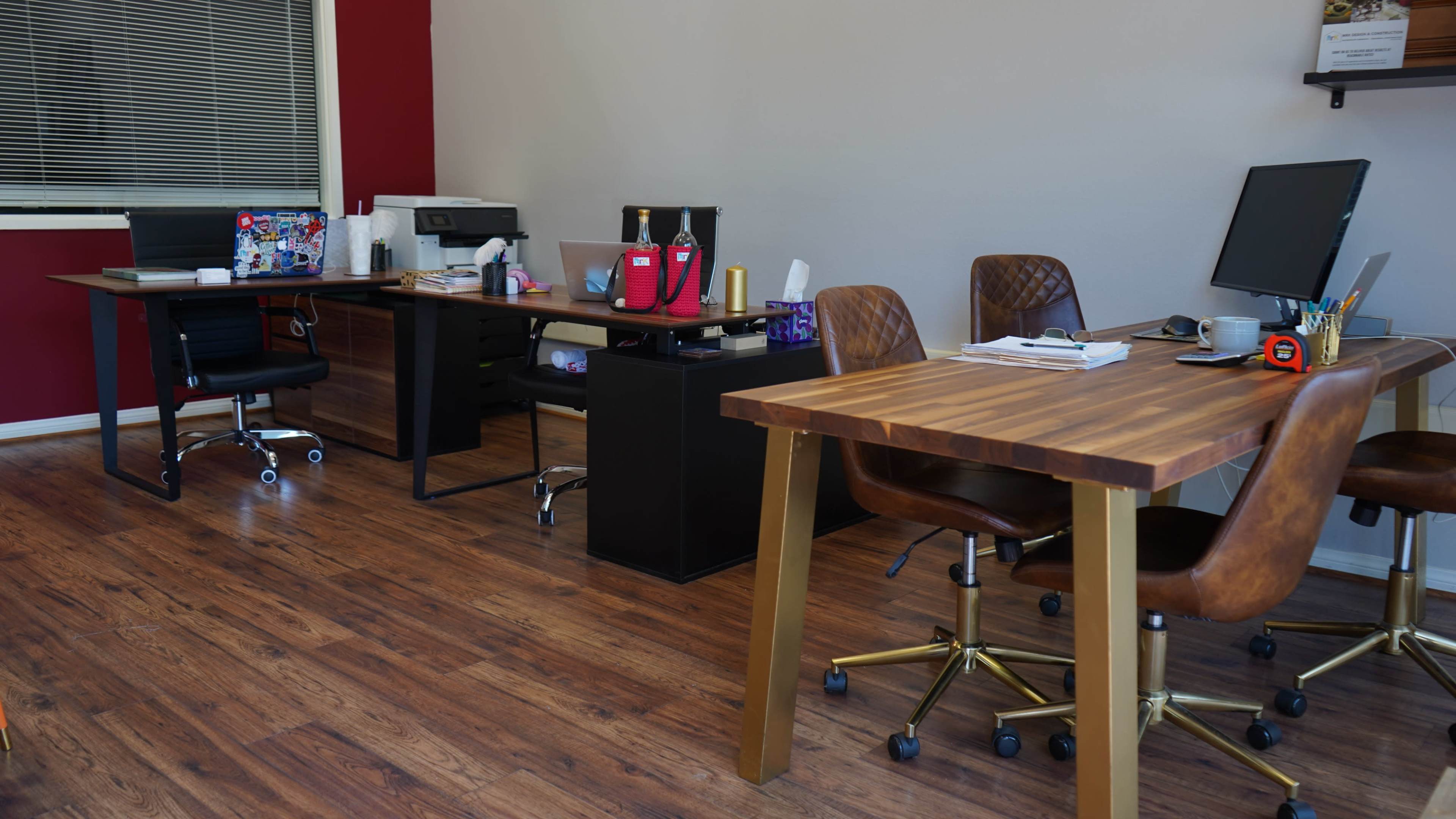 The image shows a modern office space with two desks, office chairs, and various office supplies arranged along a wooden floor.