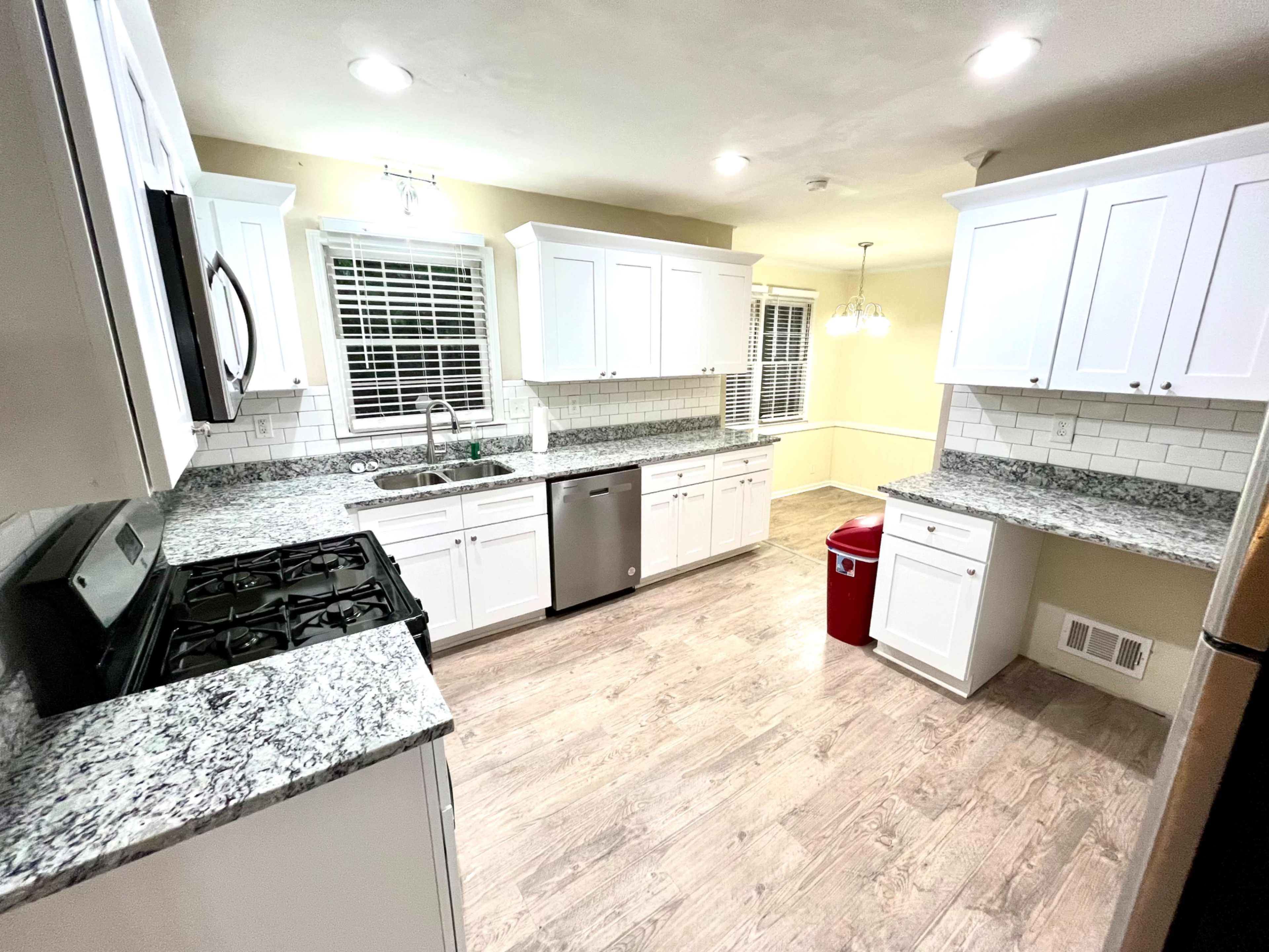 The kitchen features white cabinets, granite countertops, stainless steel appliances, and a combination of tile and wood flooring.