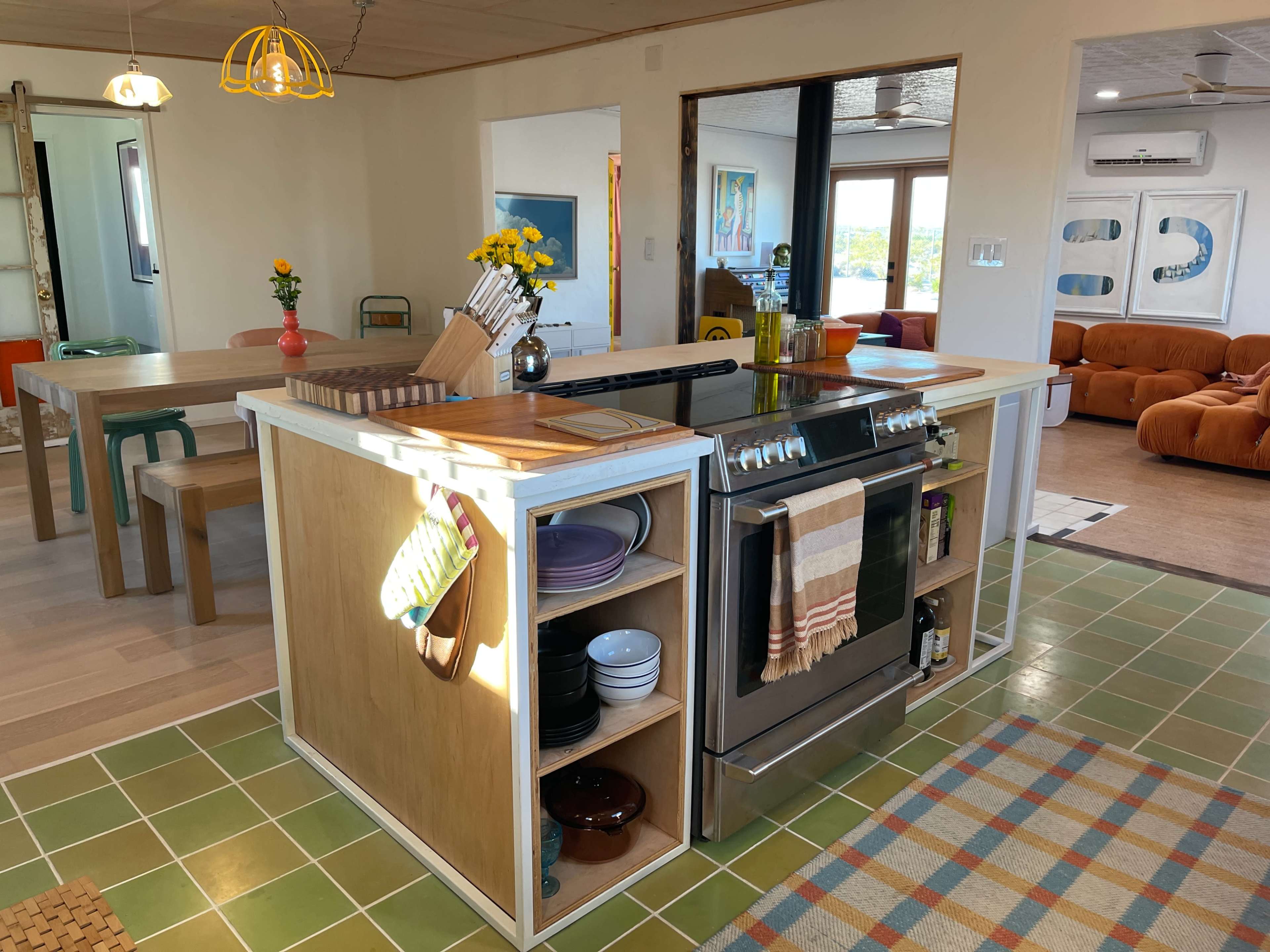 A modern kitchen with a large island featuring a stovetop, colorful dishes, and a dining area adjacent to it.