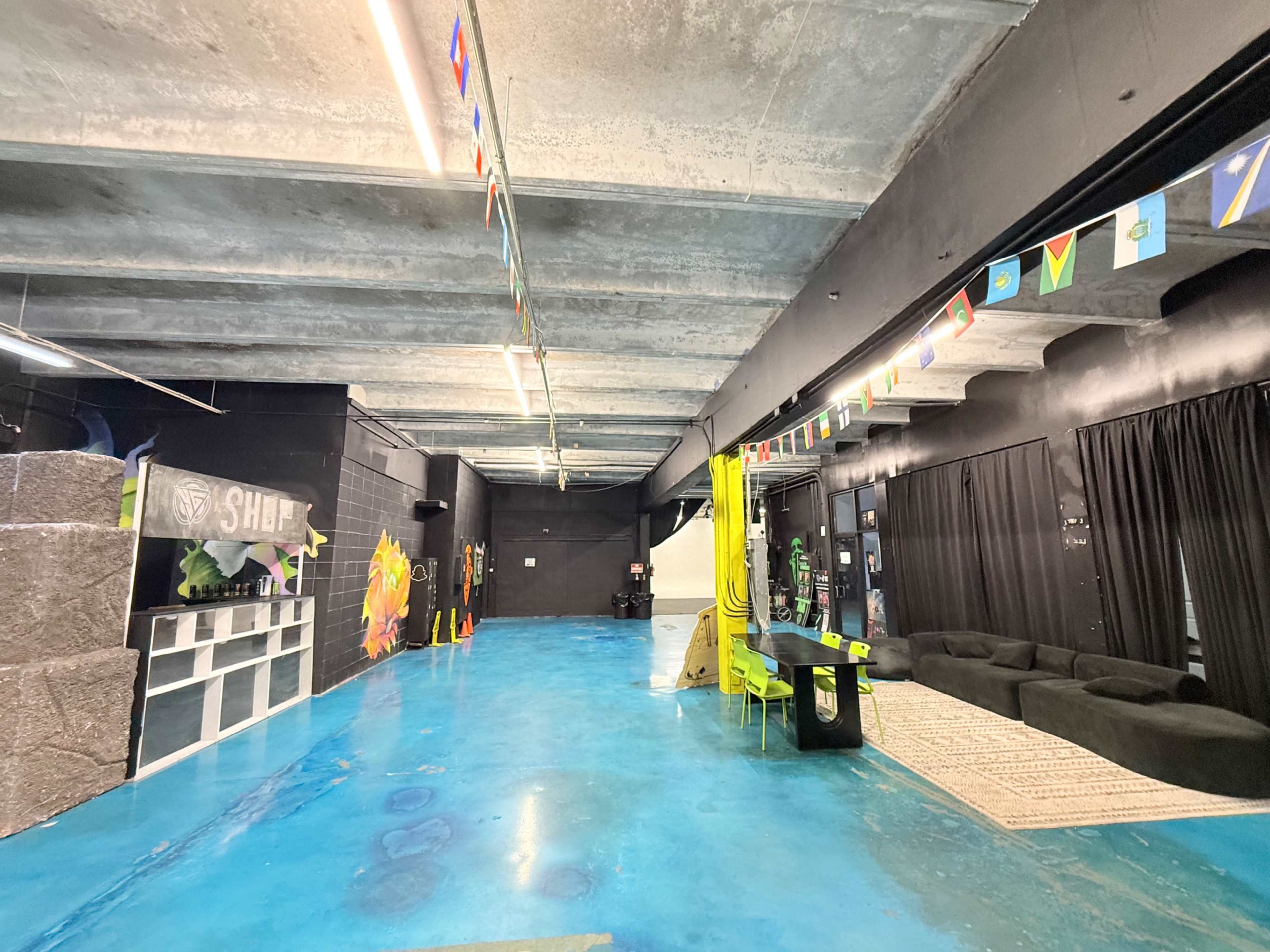 The image shows a spacious indoor area with bright blue flooring, black walls, and several decorative flags hanging from the ceiling.