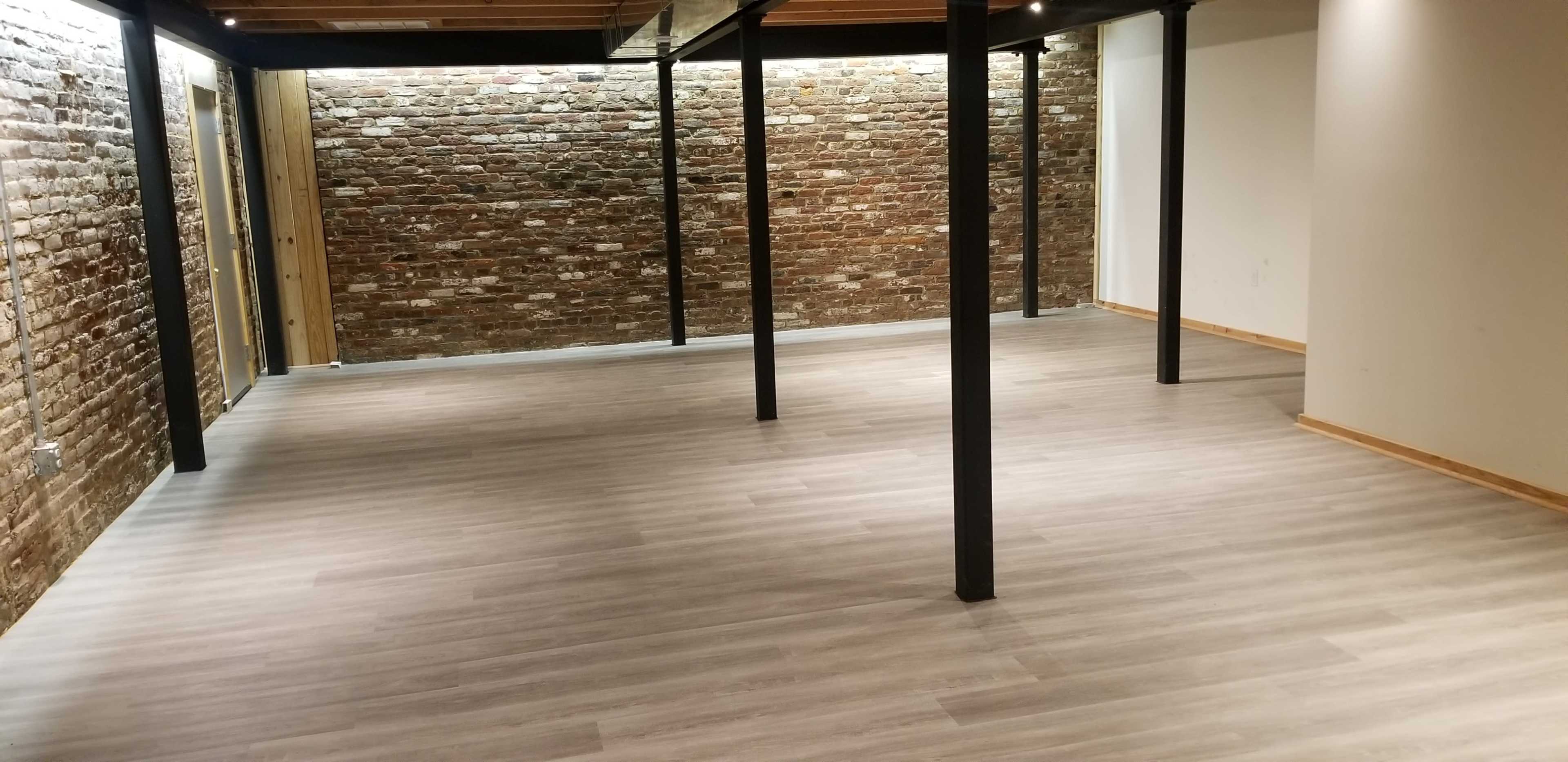 A spacious interior with a wooden floor, exposed brick walls, and metal columns.
