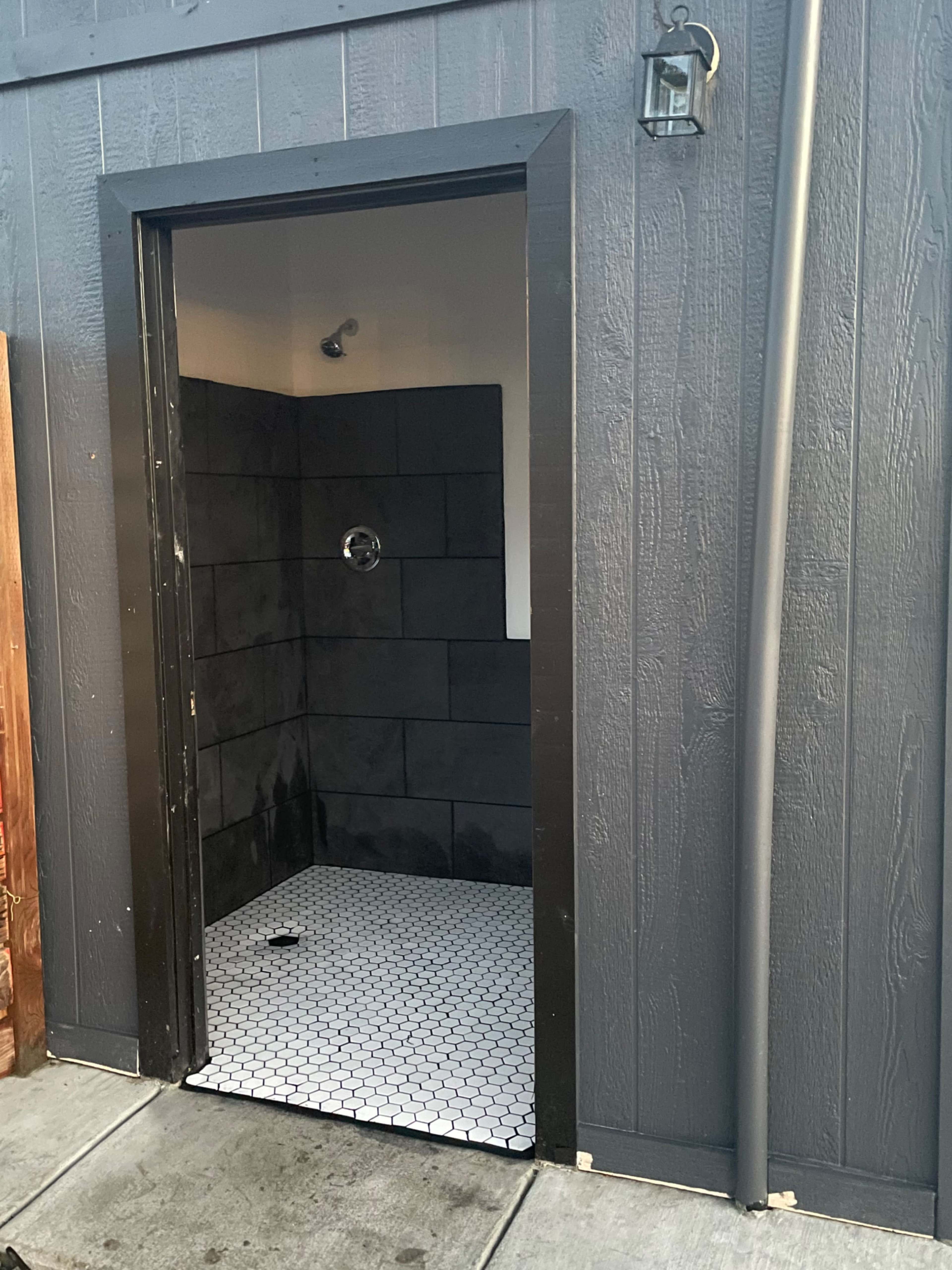 An empty outdoor shower with black tile walls and a hexagonal tiled floor.