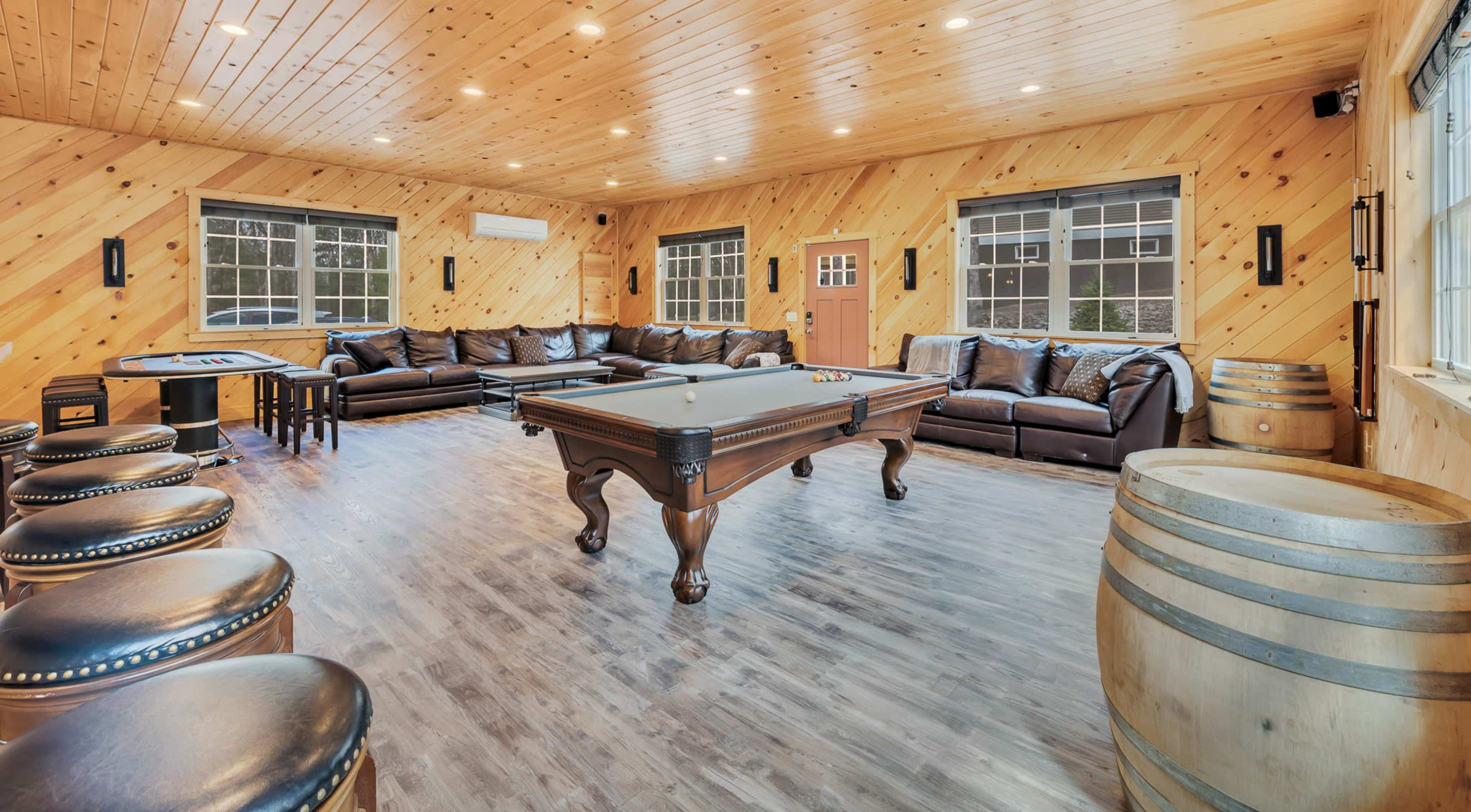 A large game room with a pool table, leather sofas, and wooden accents, illuminated by recessed lighting.