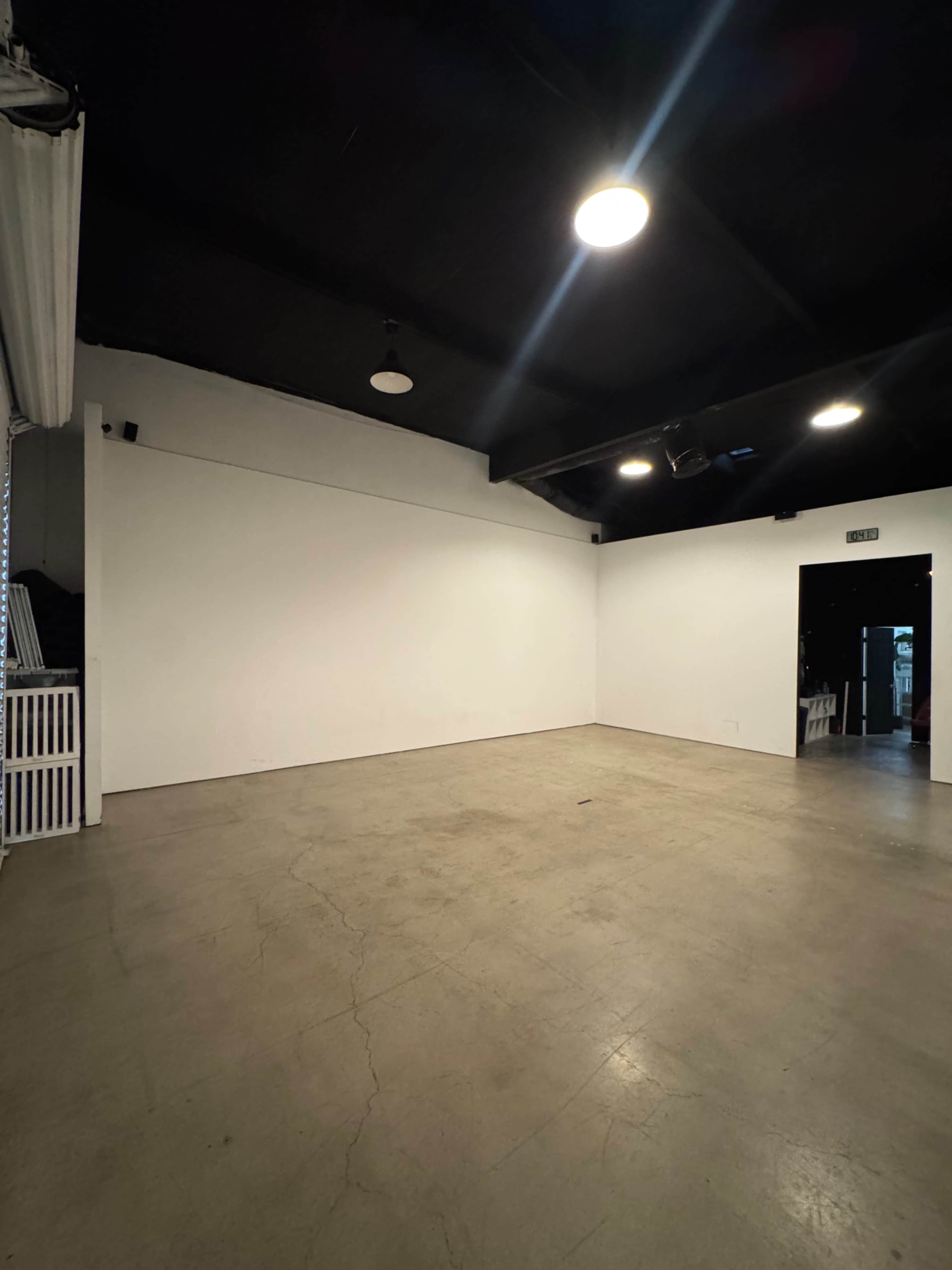 The image shows a large, empty room with a polished concrete floor and white walls, illuminated by overhead lights.