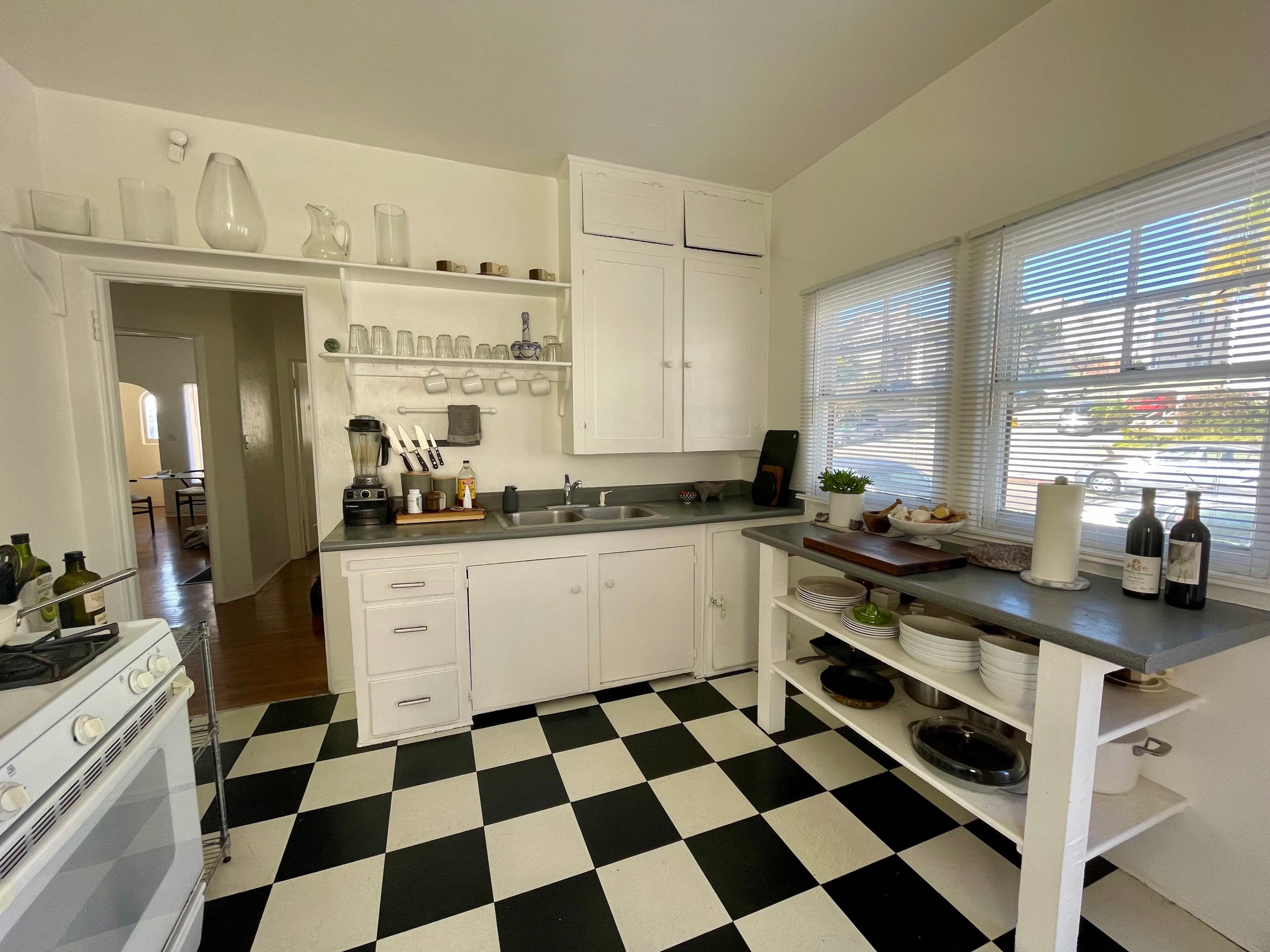 A bright kitchen featuring white cabinets, a black and white checkered floor, and a window allowing natural light to enter the space.