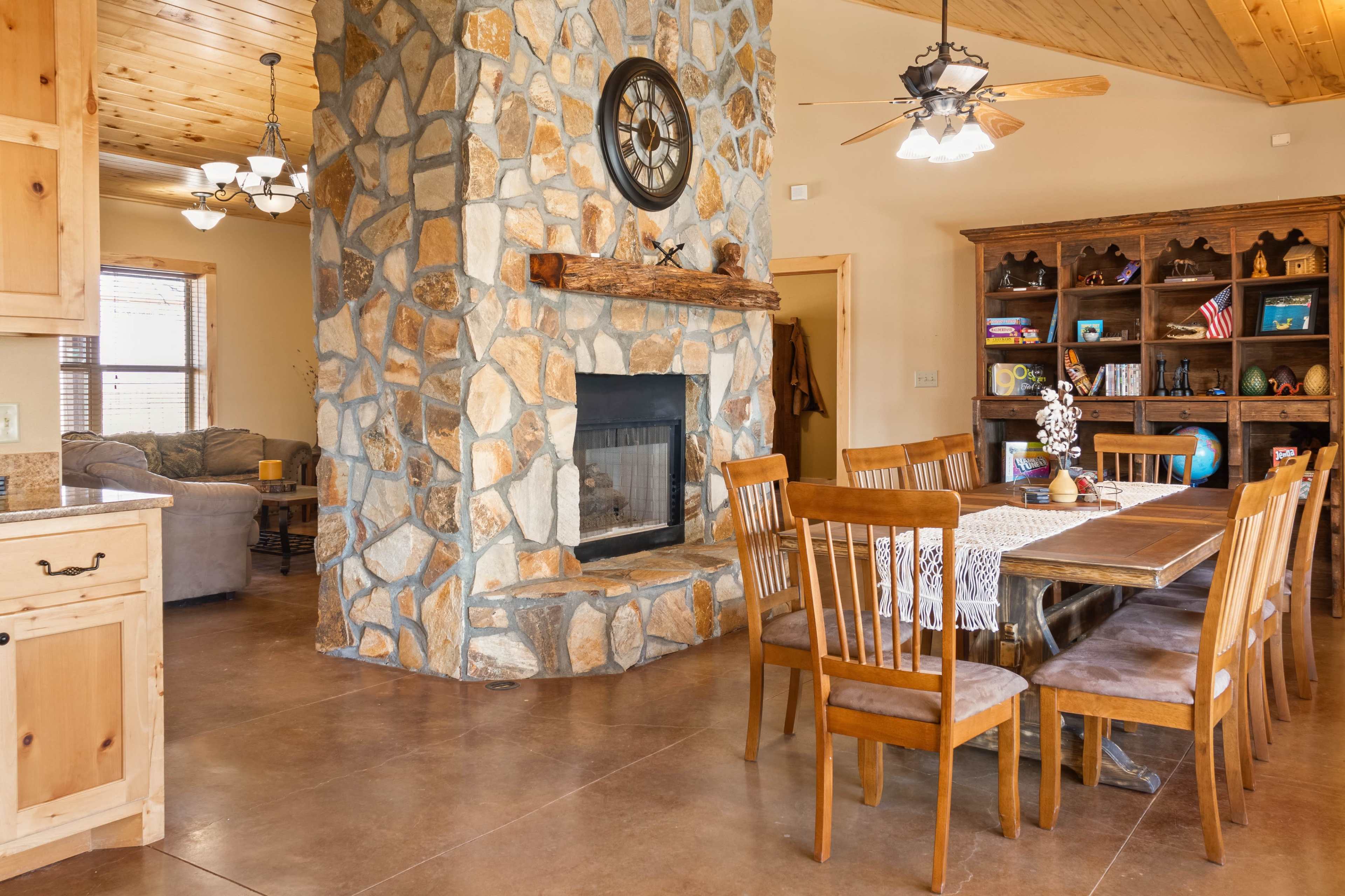 A spacious interior featuring a stone fireplace, wooden dining table with chairs, and a cozy living area in the background.