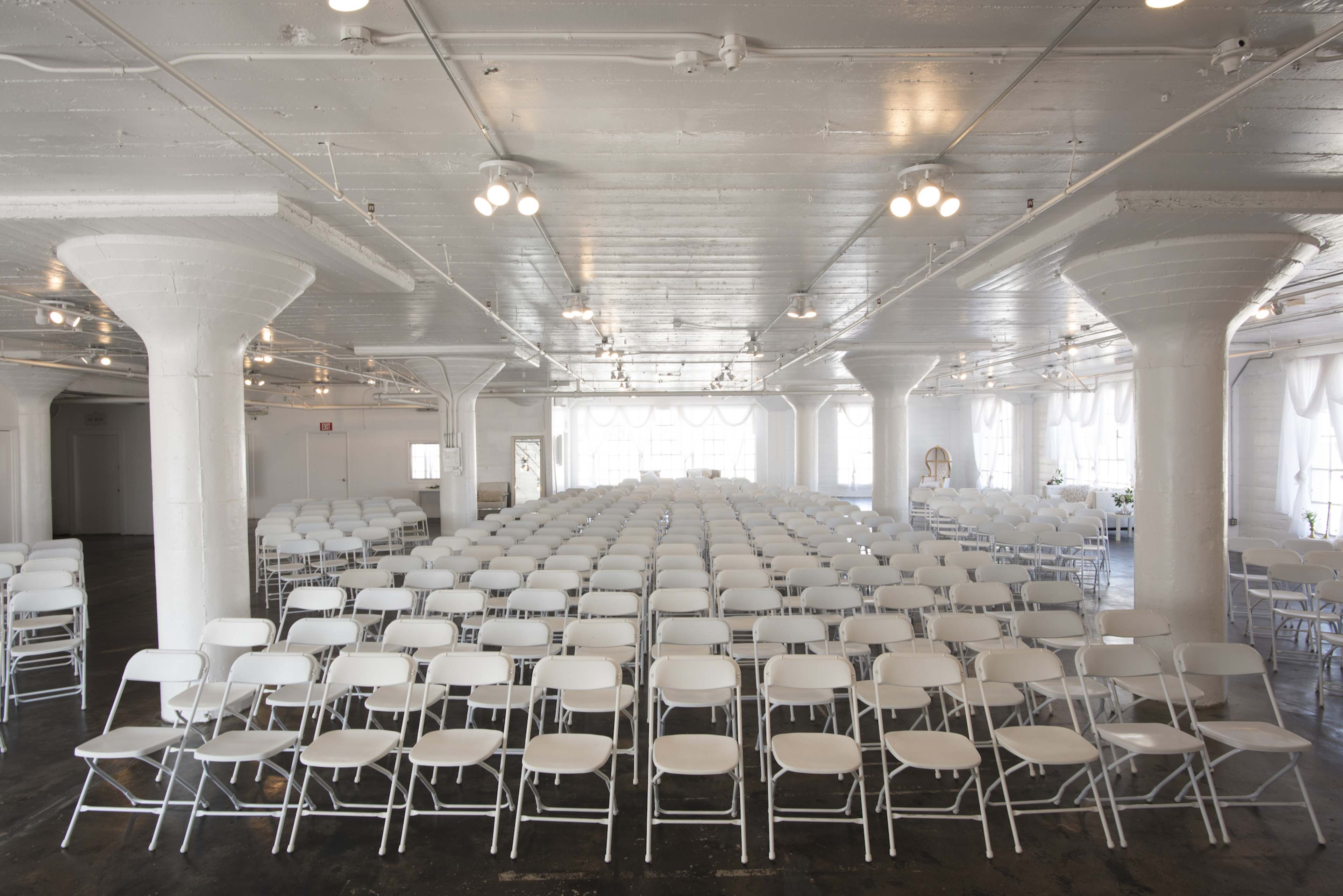 A large, empty hall filled with rows of white folding chairs arranged neatly in front of a simple backdrop.