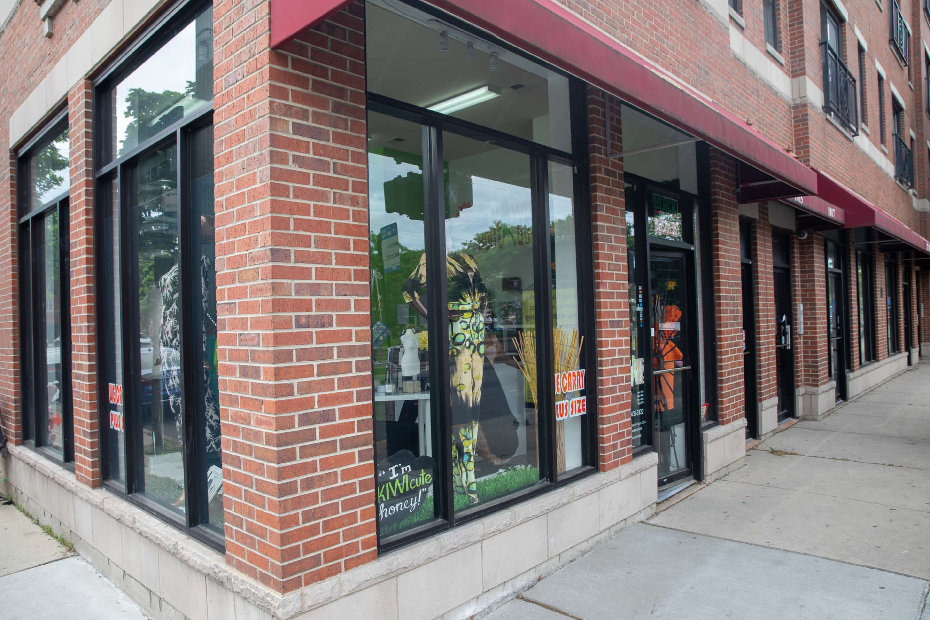 The image shows a storefront with large glass windows displaying various colorful items and signage in a brick building.