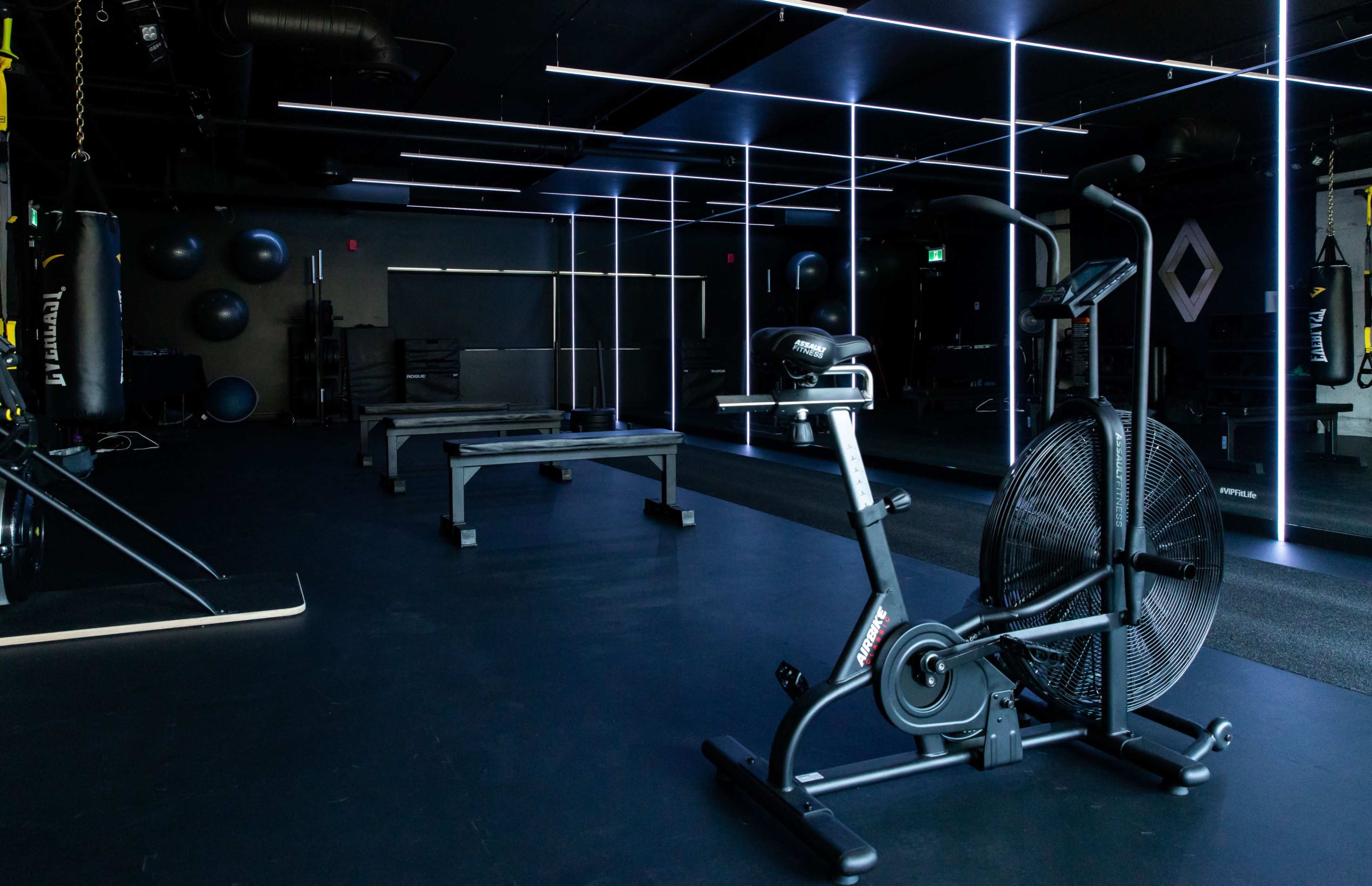 A stationary exercise bike is positioned in a dimly lit gym featuring modern equipment and illuminated lines.