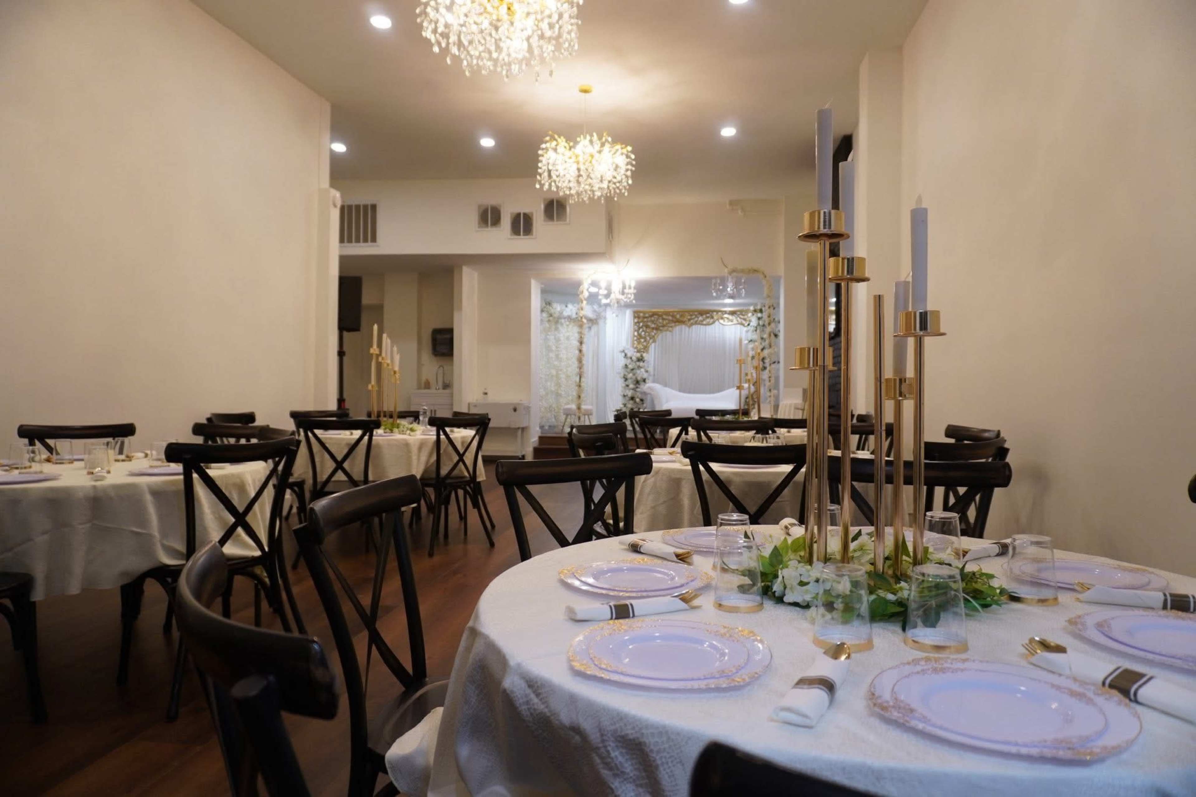 The image shows a dining area with round tables set with elegant tableware and decorative centerpieces, illuminated by soft lighting from chandeliers.