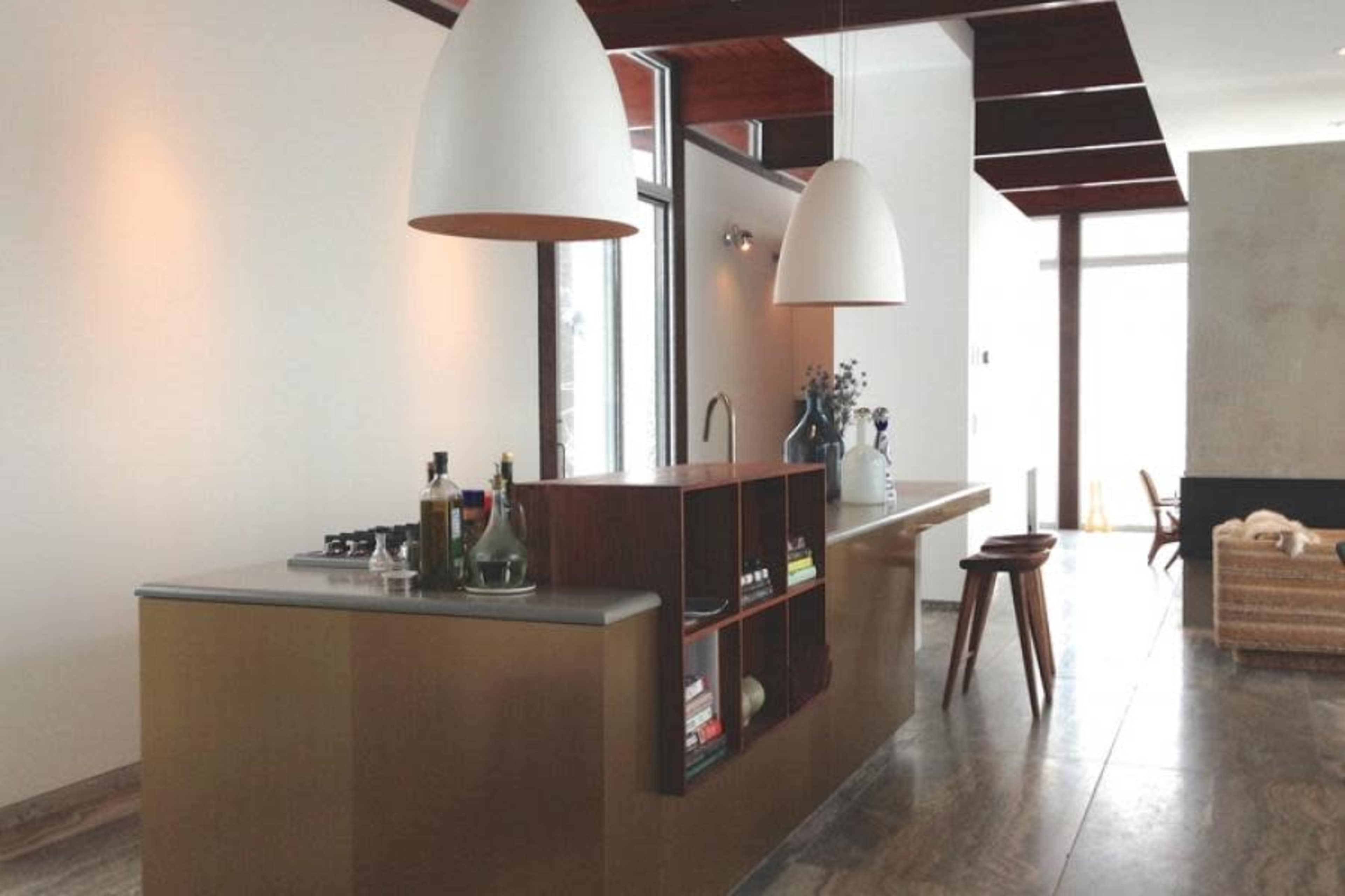 A modern kitchen features a sleek island with a countertop, shelving for books, and two large pendant lights hanging above.
